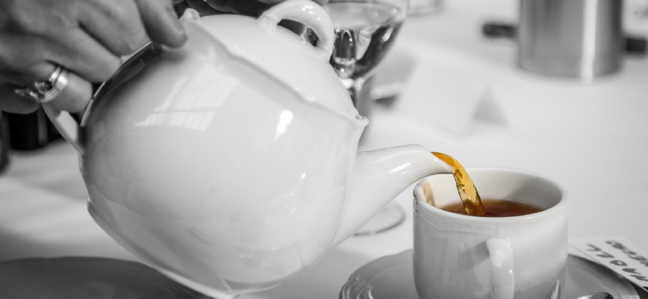 Tetera de porcelana blanca sirviendo licor de té dorado en una taza de cata