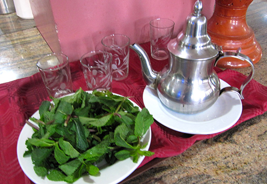 Tetera de metal tradicional, vasitos de vidrio y plato con abundante menta fresca