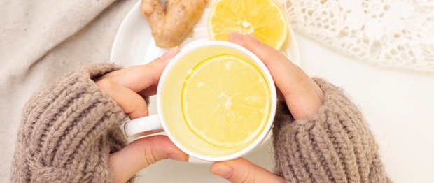 Manos sosteniendo una taza de té tibio con rodaja de limón y jengibre