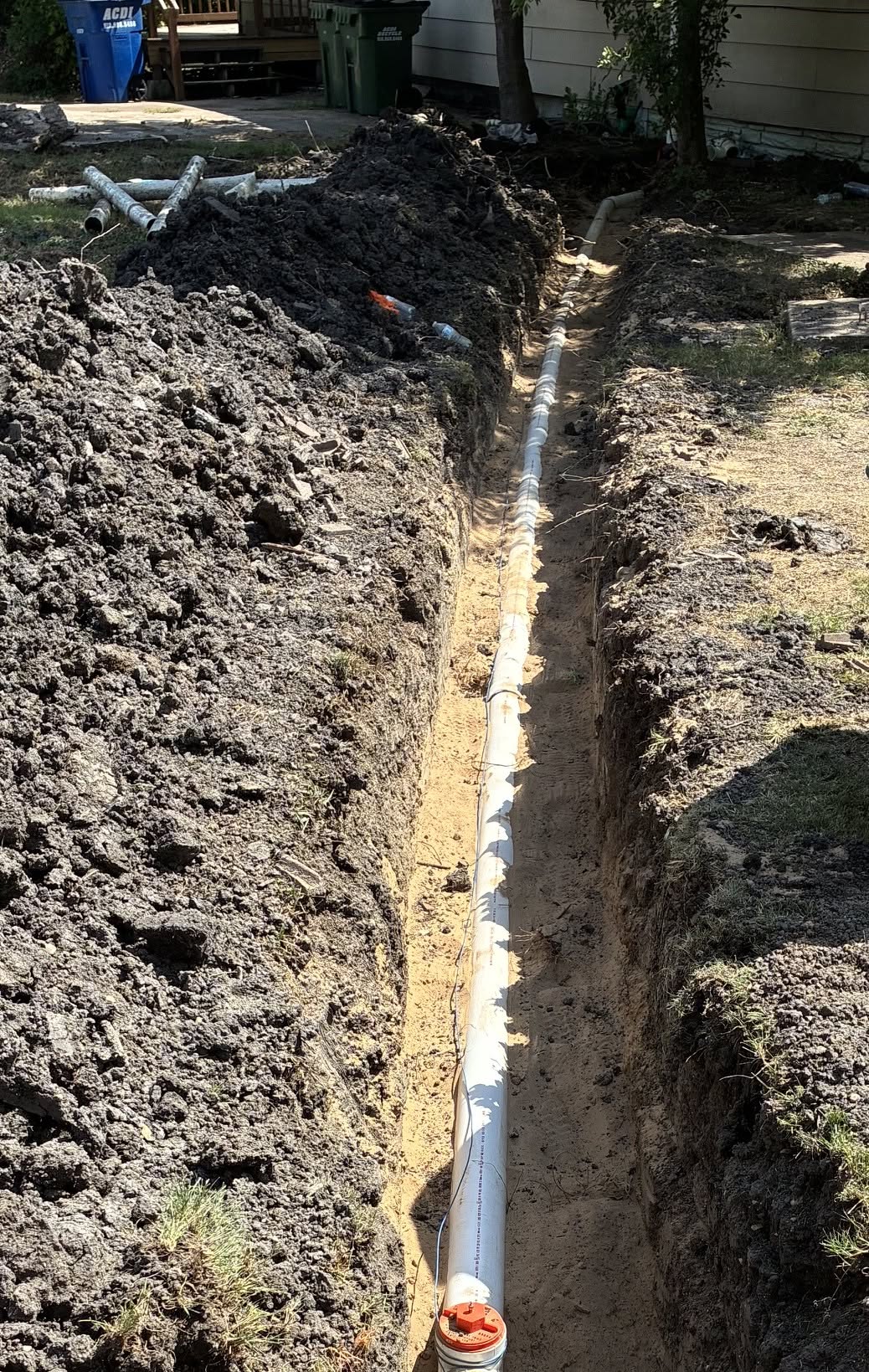Deep excavated trench showing new PVC sewer main line bedded in sand with cleanout in foreground