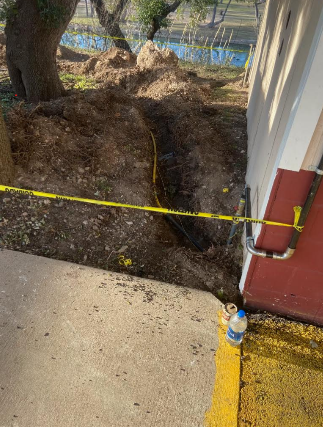 Underground gas line trench showing yellow poly pipe transitioning to riser at building exterior