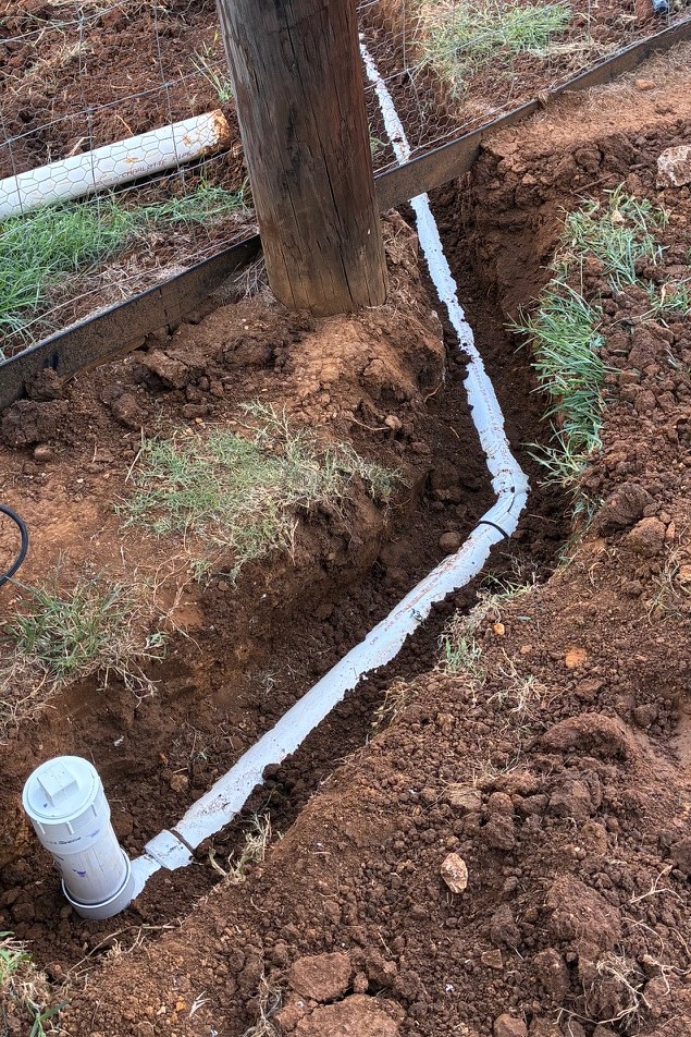 New white PVC sewer line replacement laid with cleanout installed along trench on a Central Texas property