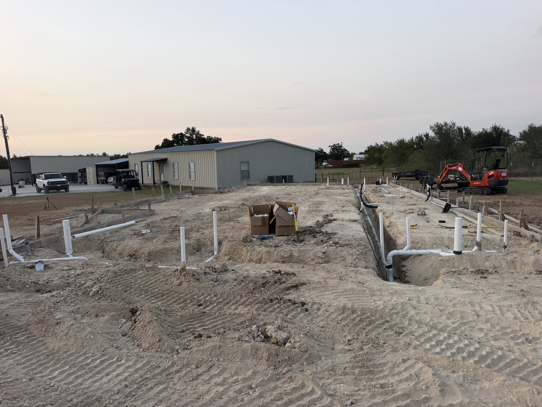 Wide view of new construction building pad with plumbing trenches and PVC risers set for foundation pour