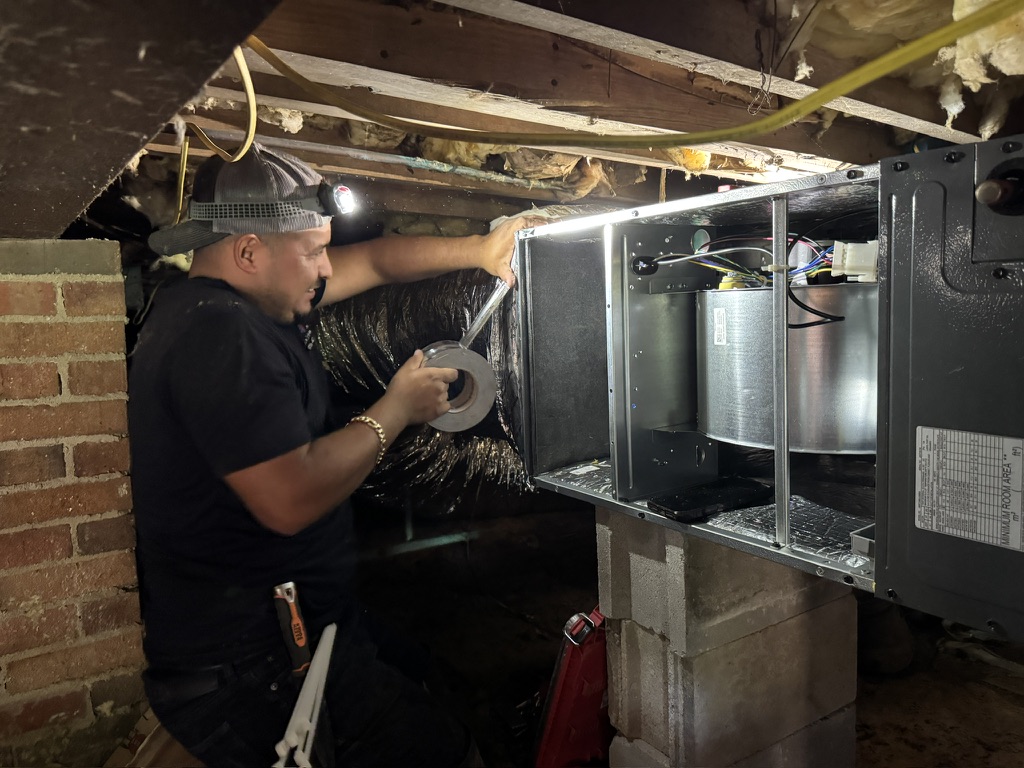Oscar Aguirre servicing an indoor air handler unit inside a crawl space
