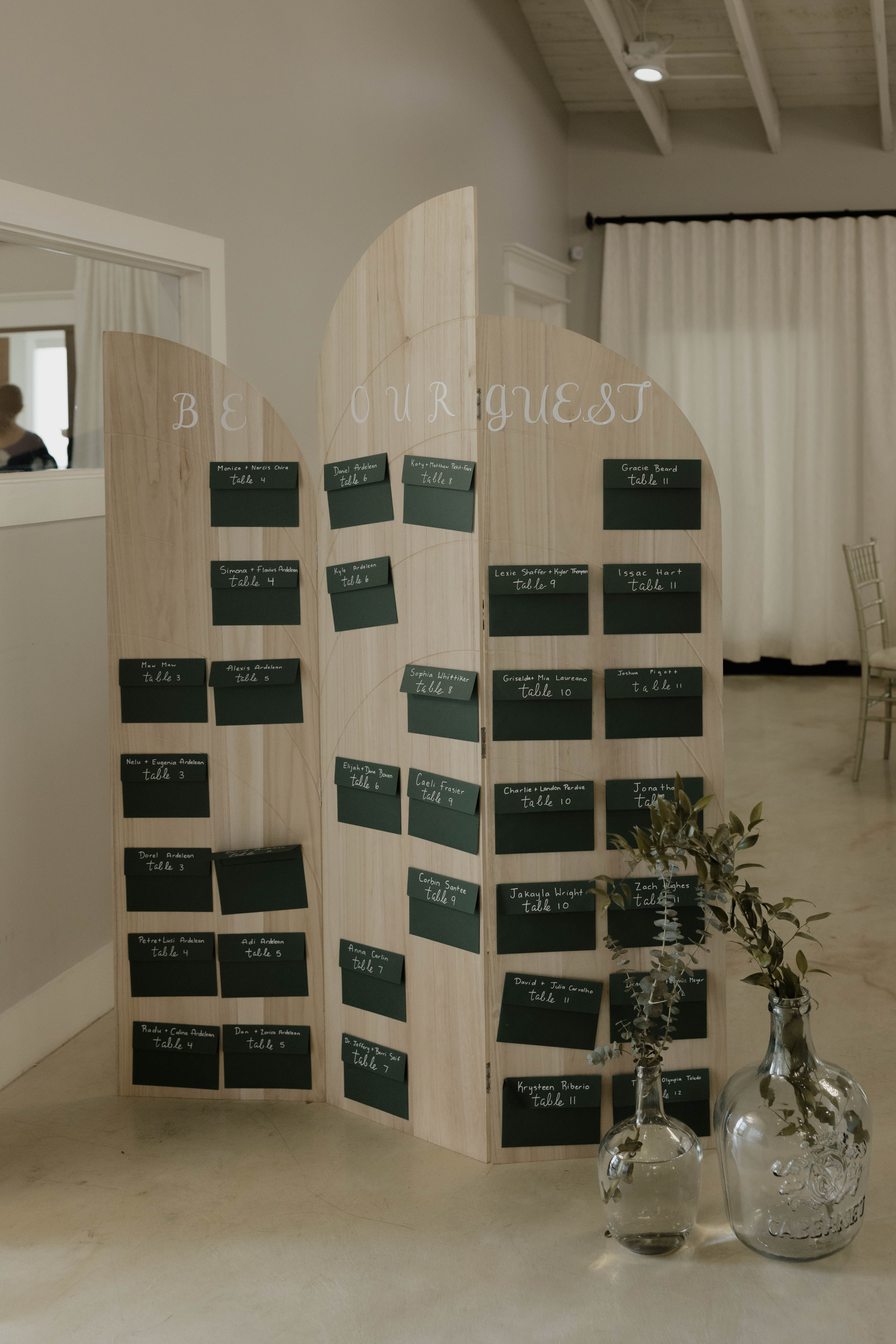 HoneyBee Events custom arched wooden seating chart display with dark green escort envelopes and botanical styling