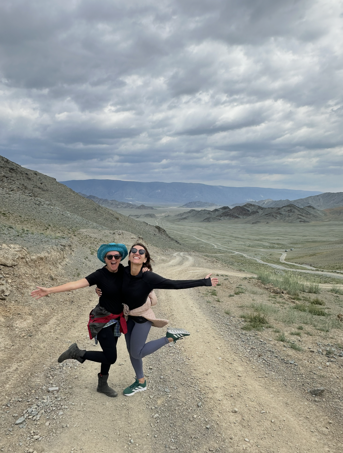 Two women smiling with open arms celebrating on a scenic dirt road mountain adventure