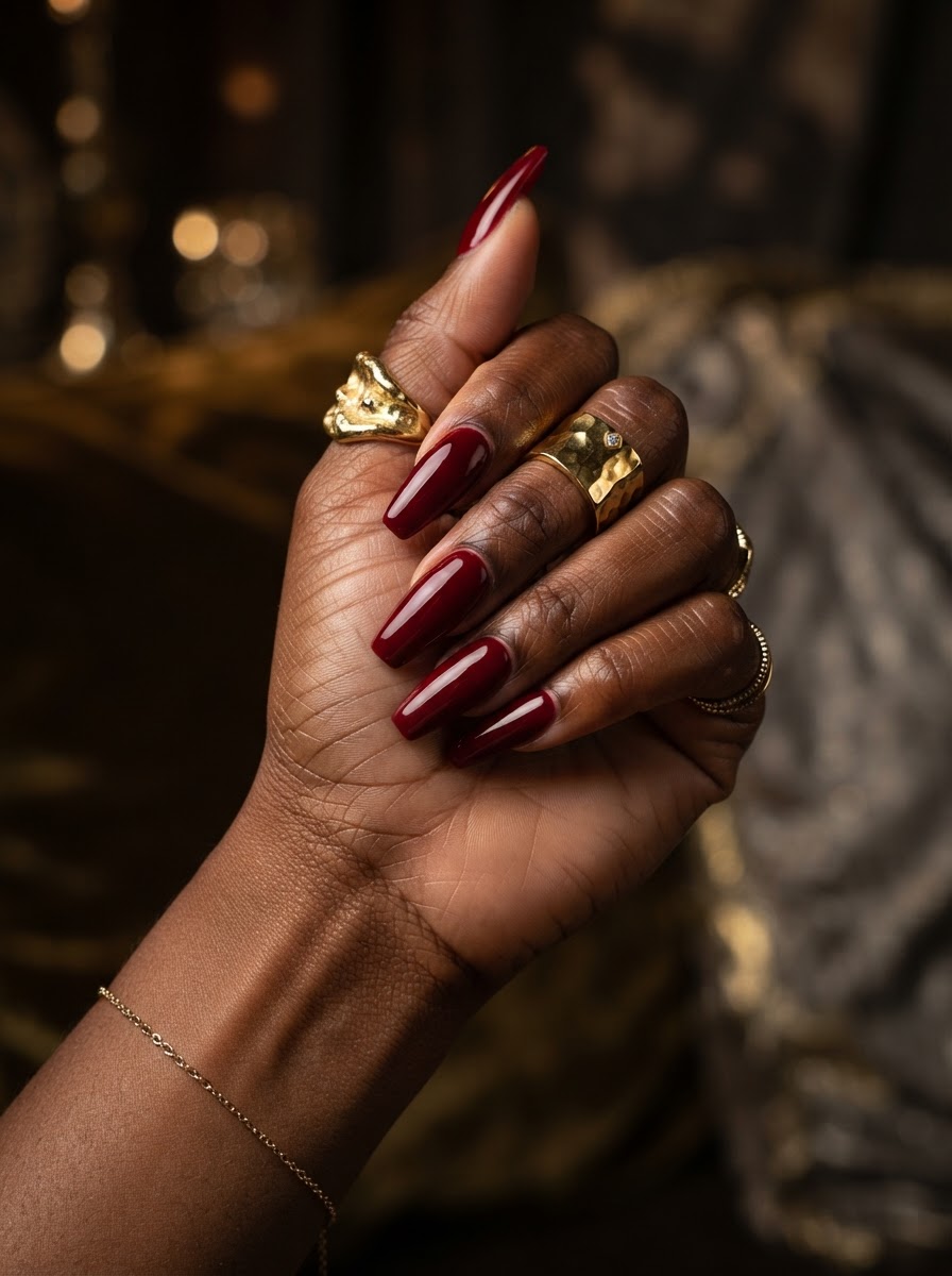 Deep glossy red manicure on a Black woman's hand with gold rings