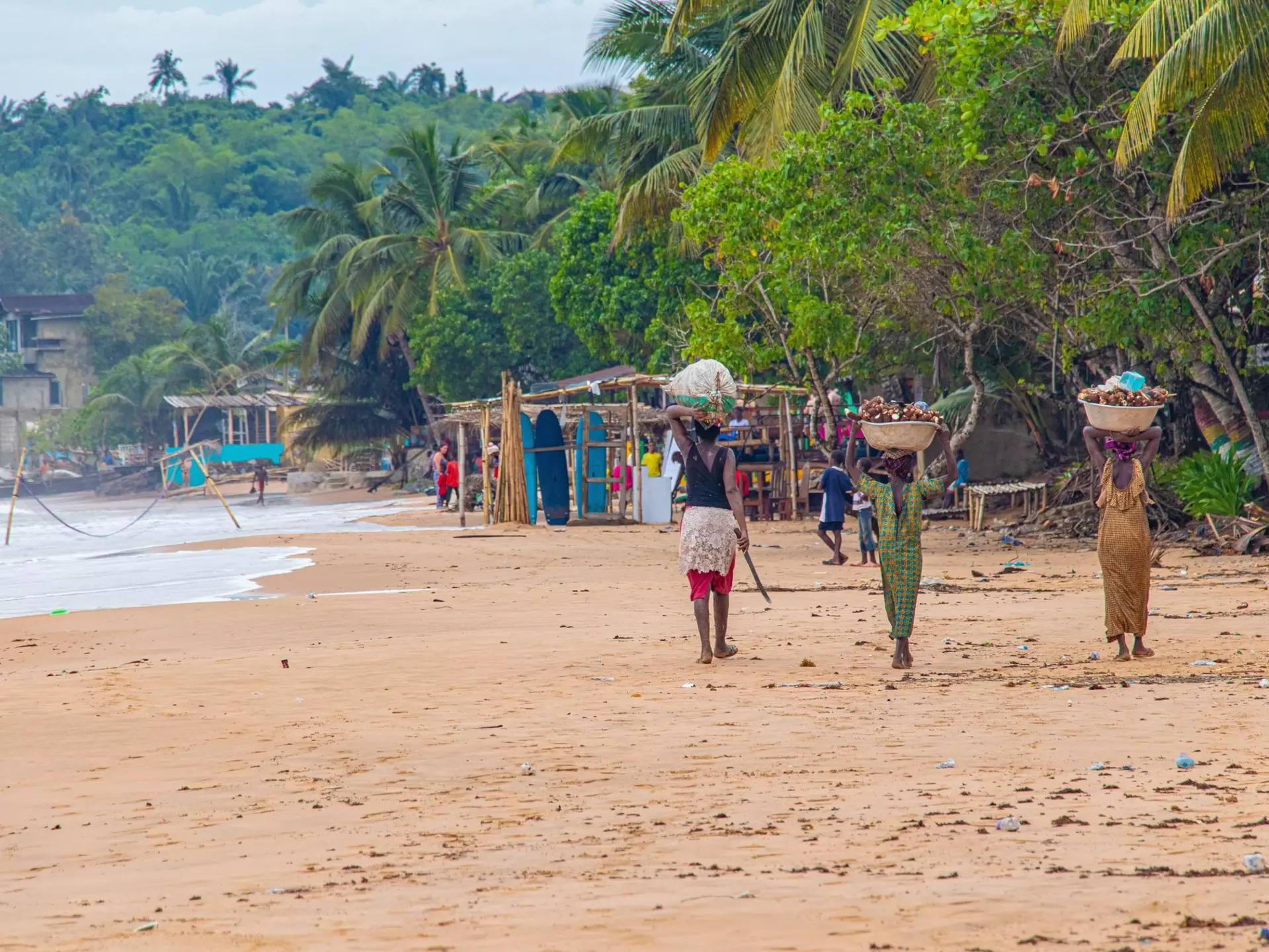 Local Ghanaian community walking the golden sands of the coast under swaying palms