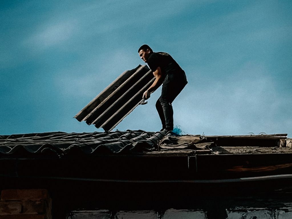 Roofer carrying a bundle of shingles across a tear-off deck at dusk