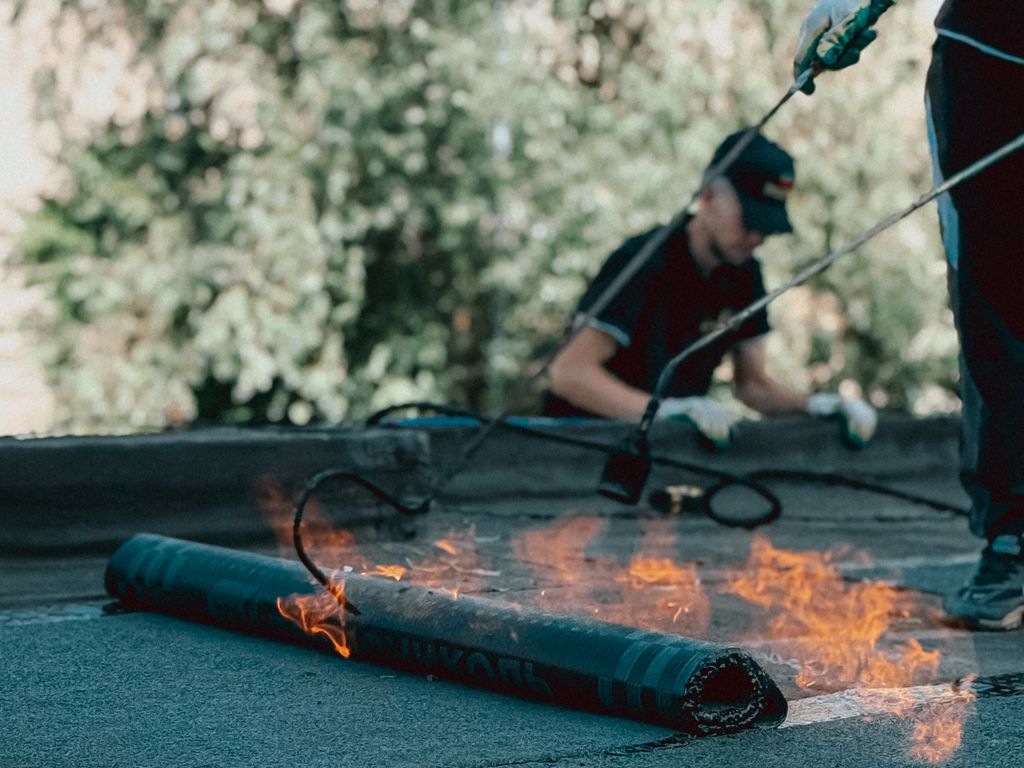 Roofer torch-applying modified bitumen membrane on a flat roof