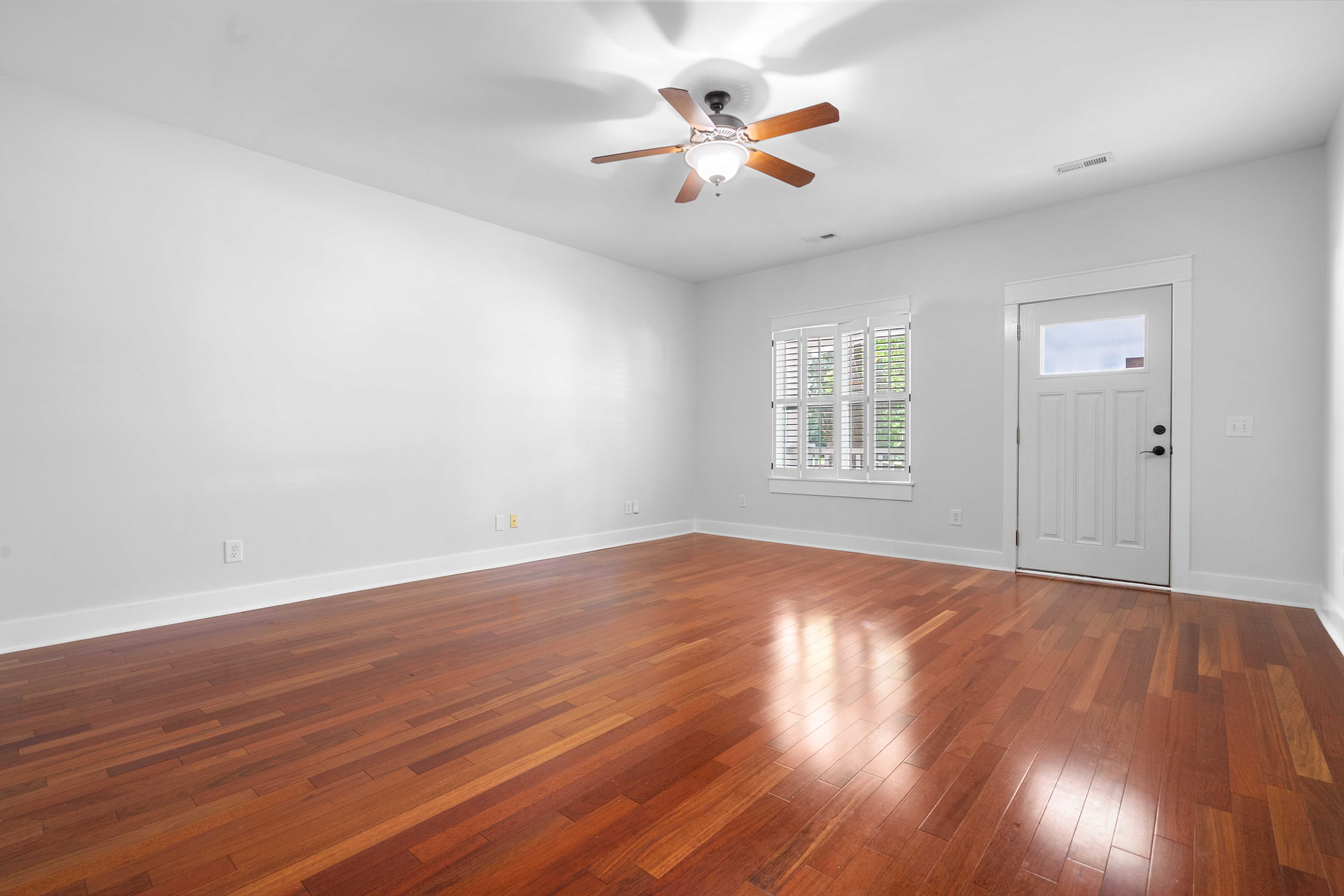 Vacant unfurnished living room with hardwood floors, ceiling fan, and entry door before virtual staging