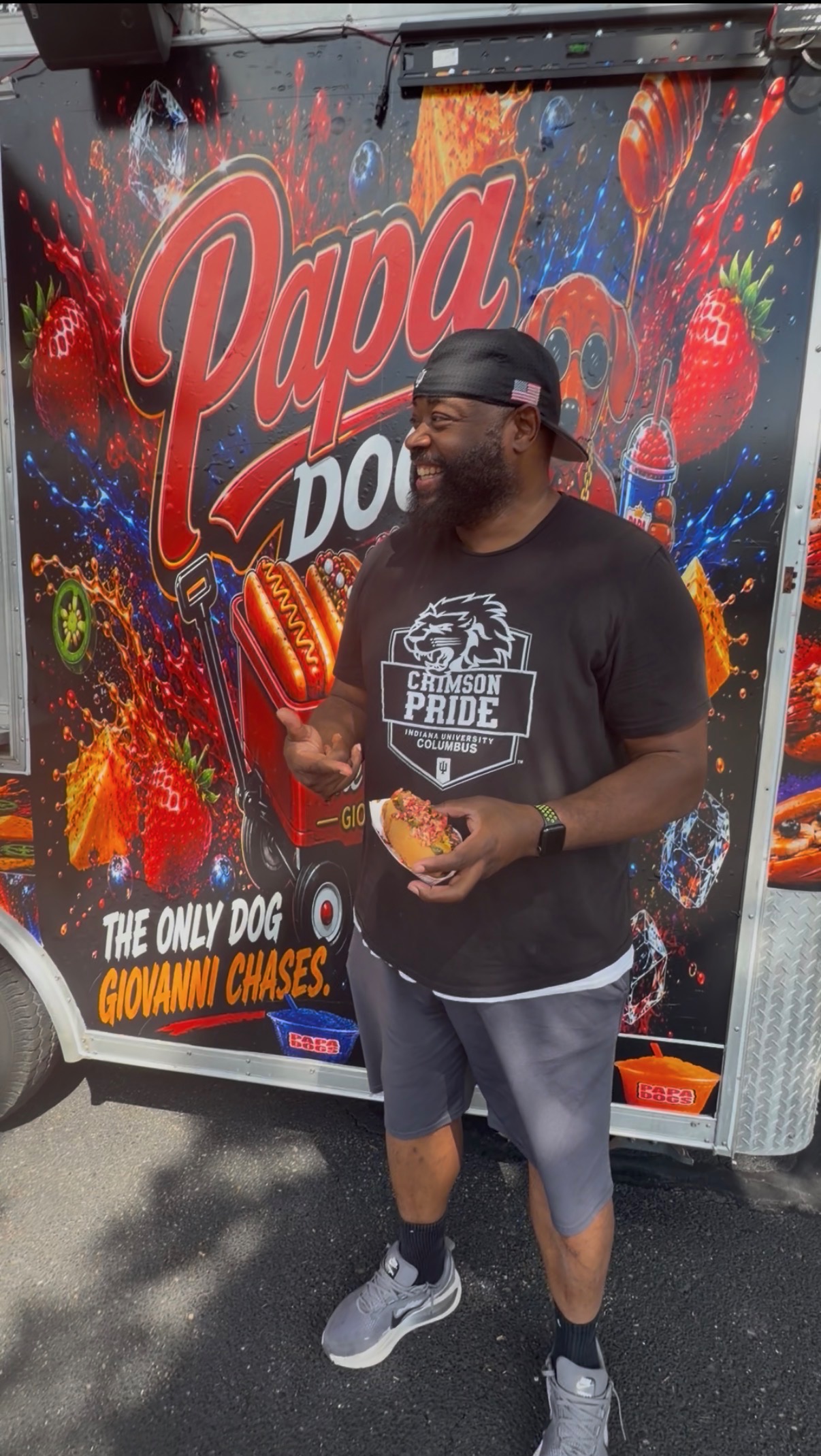 Customer laughing while holding a loaded hot dog in front of the Papa Dogs trailer mural