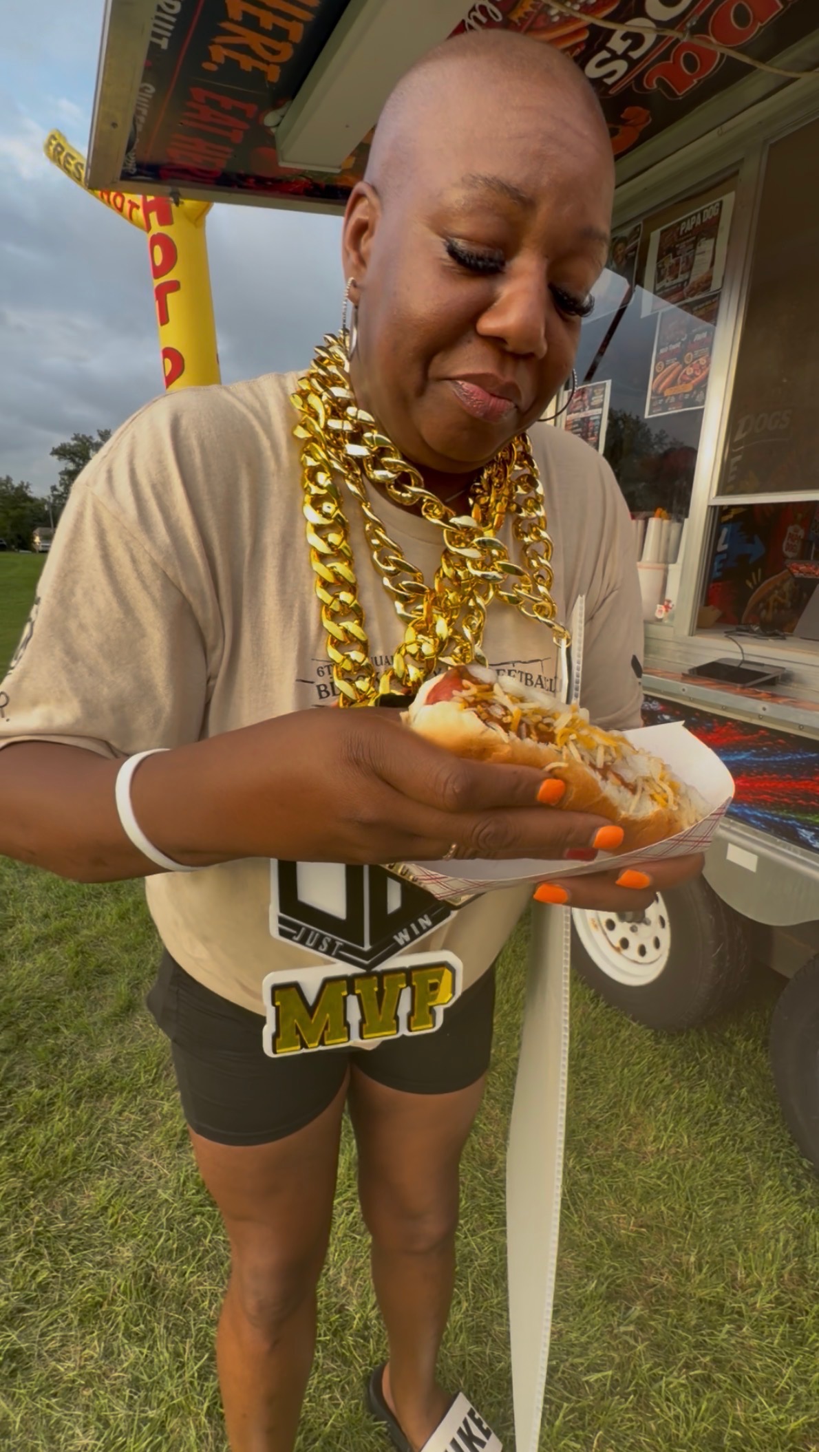 Customer with gold chains holding a loaded chili cheese hot dog