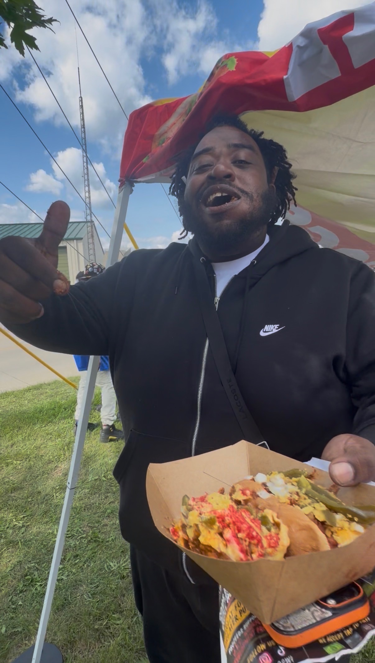 Customer giving a thumbs up while holding a loaded Papa Dogs hot dog under the tent