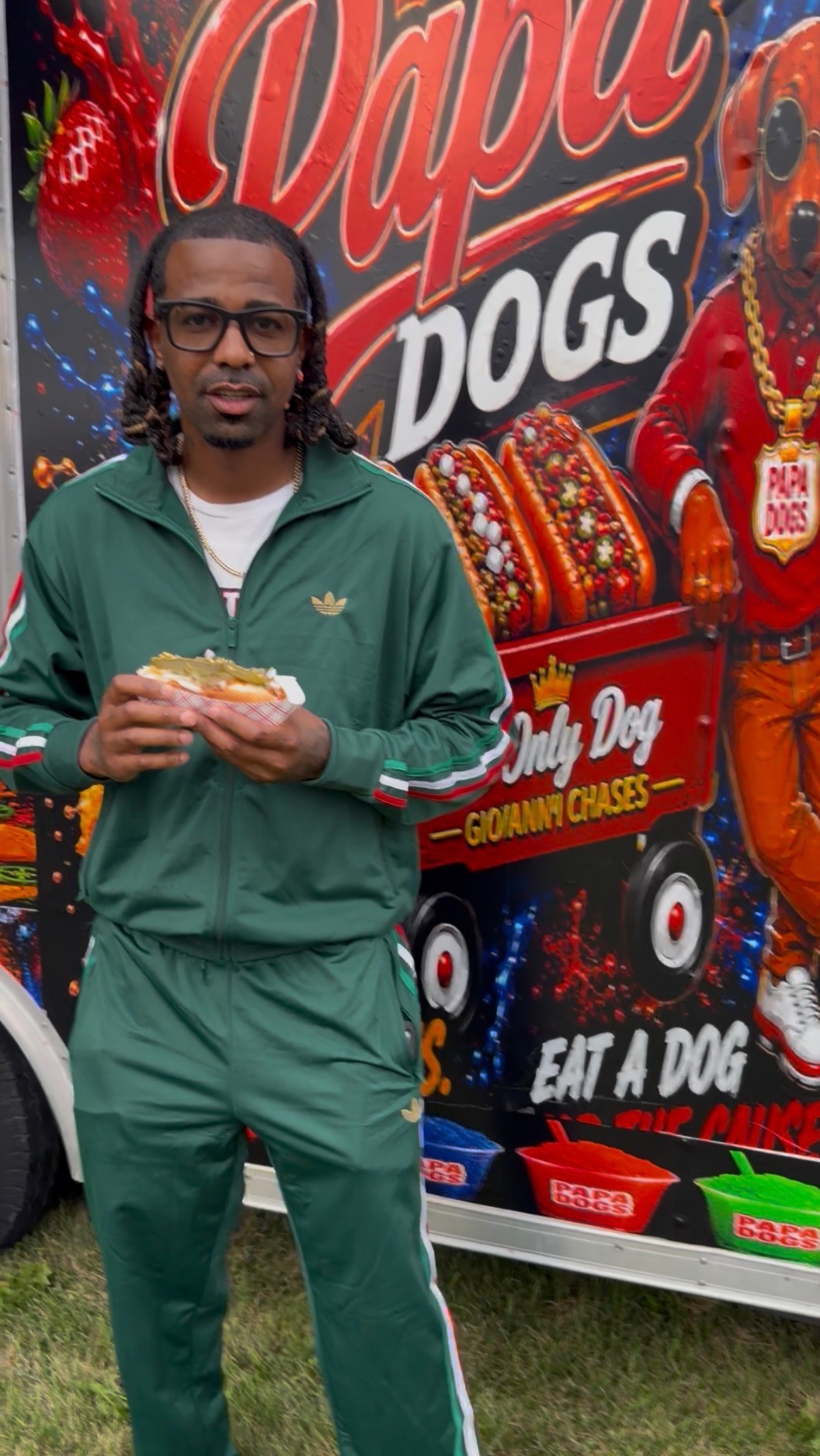 Customer in a green tracksuit holding a loaded hot dog in front of the Papa Dogs trailer
