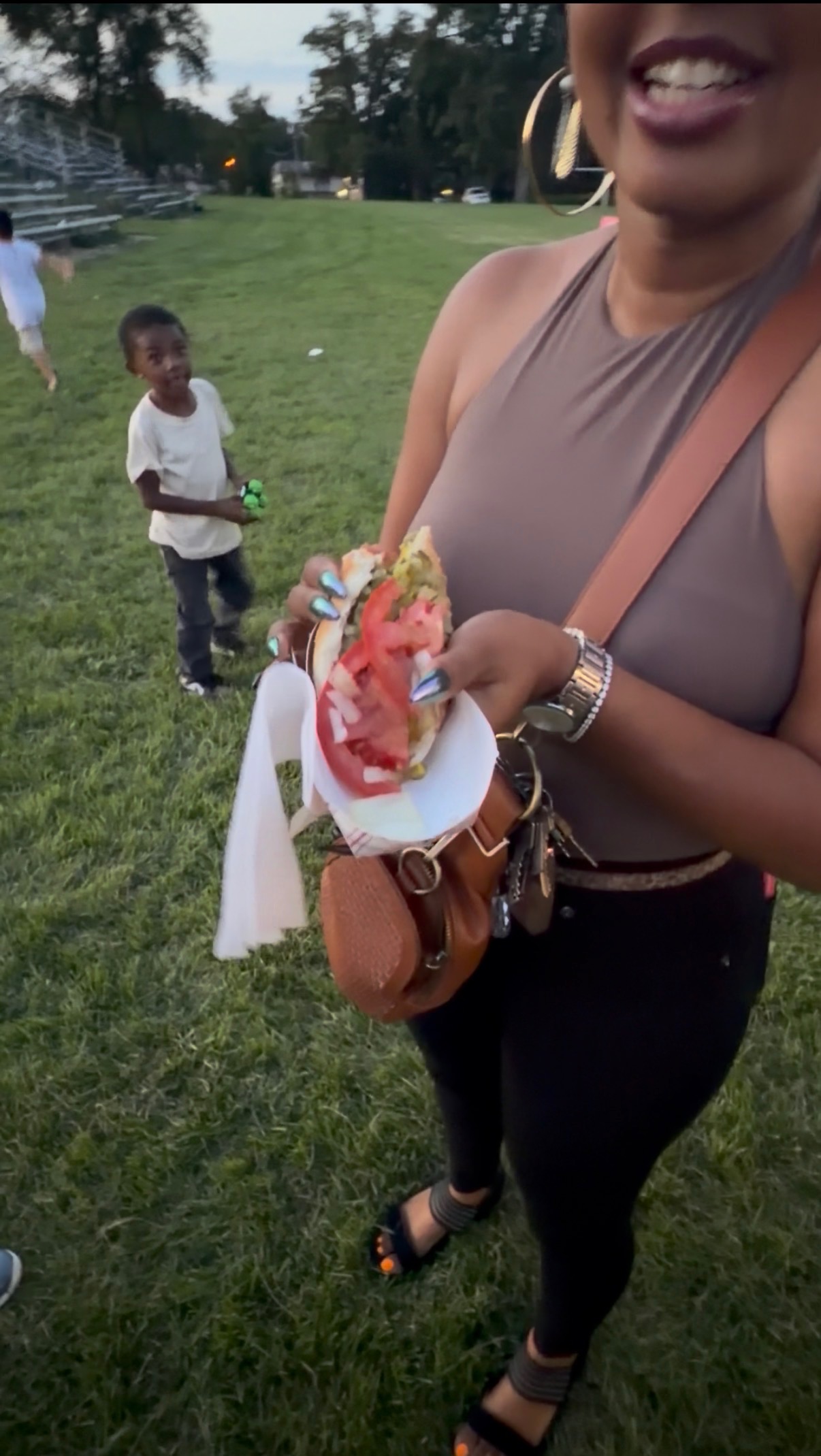 Customer holding a freshly made loaded dog with fresh tomatoes and toppings outdoors