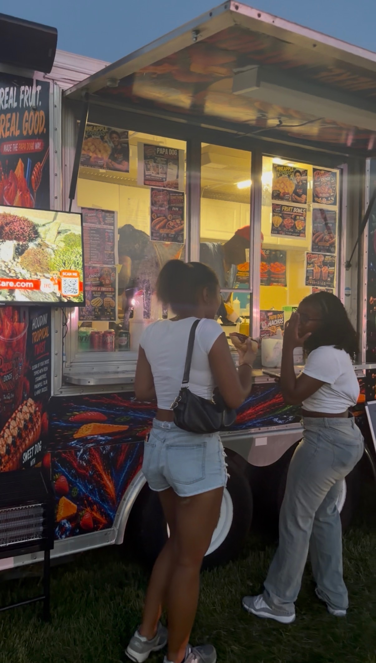 Customers ordering at the Papa Dogs trailer window in the evening