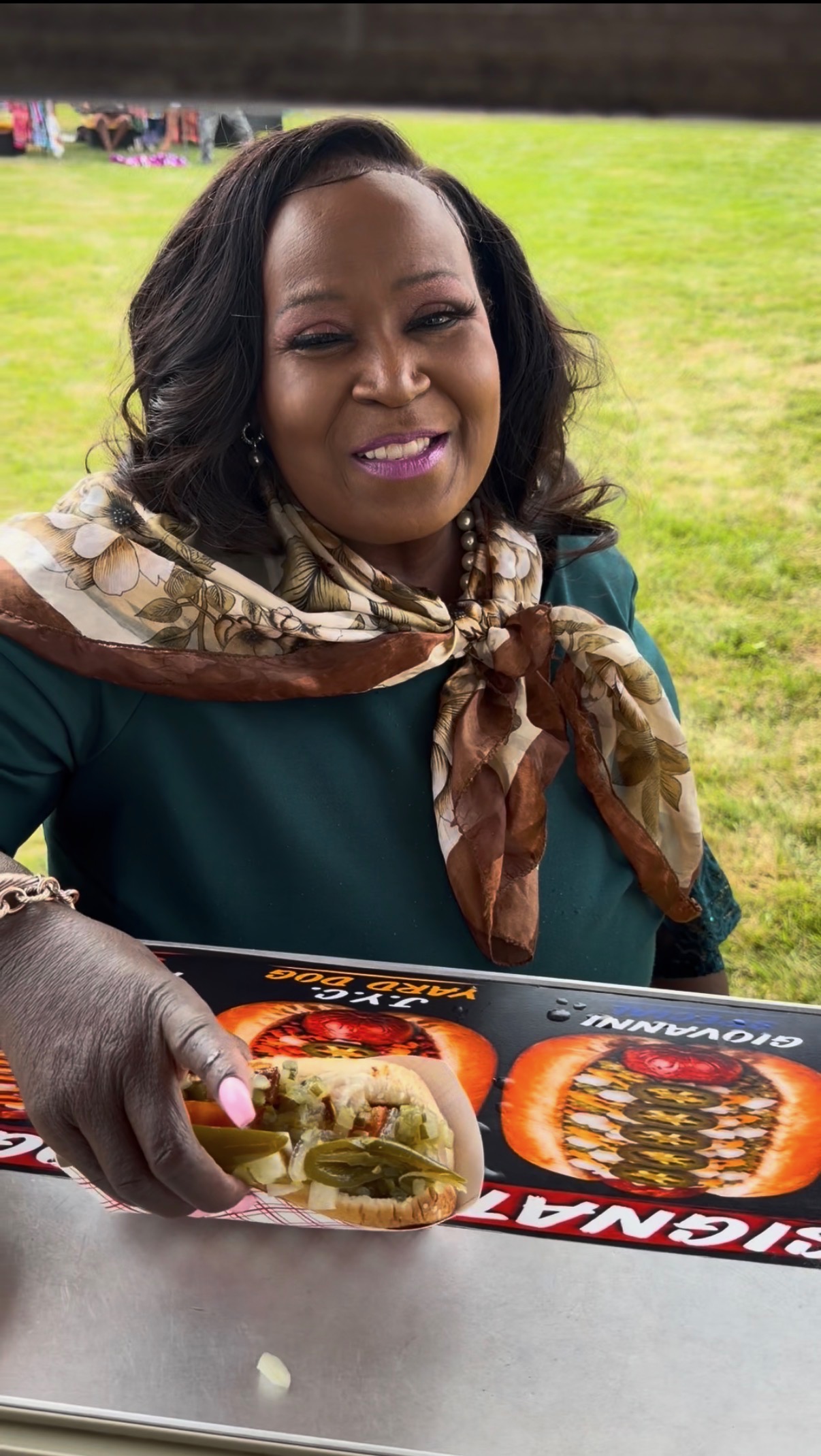 Customer in a floral scarf smiling while holding a J.Y.C. Yard Dog at the Papa Dogs trailer
