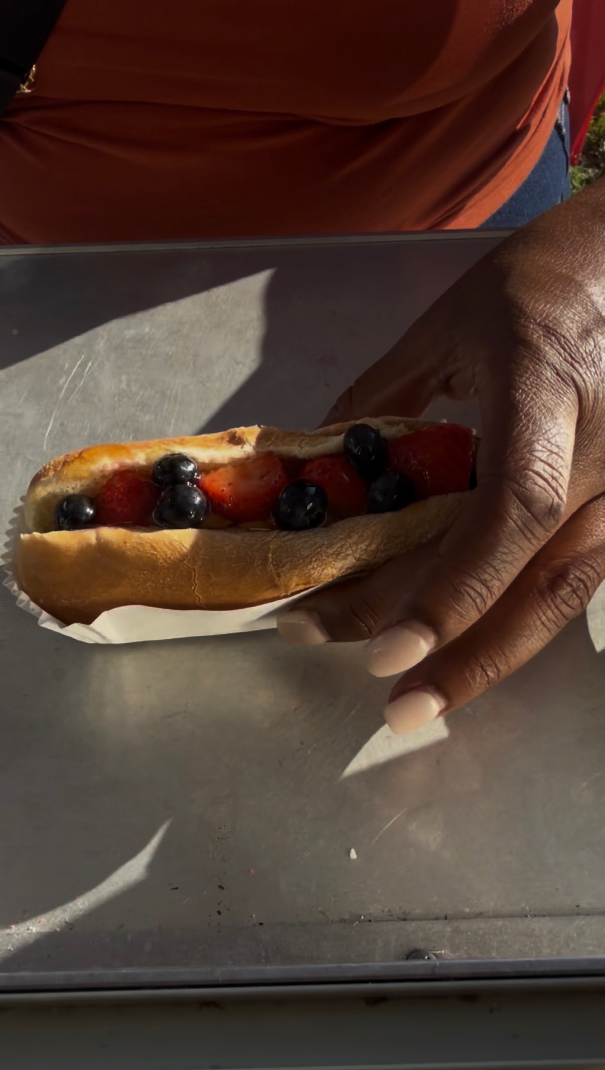 Customer holding a sweet hot dog topped with fresh strawberries and blueberries