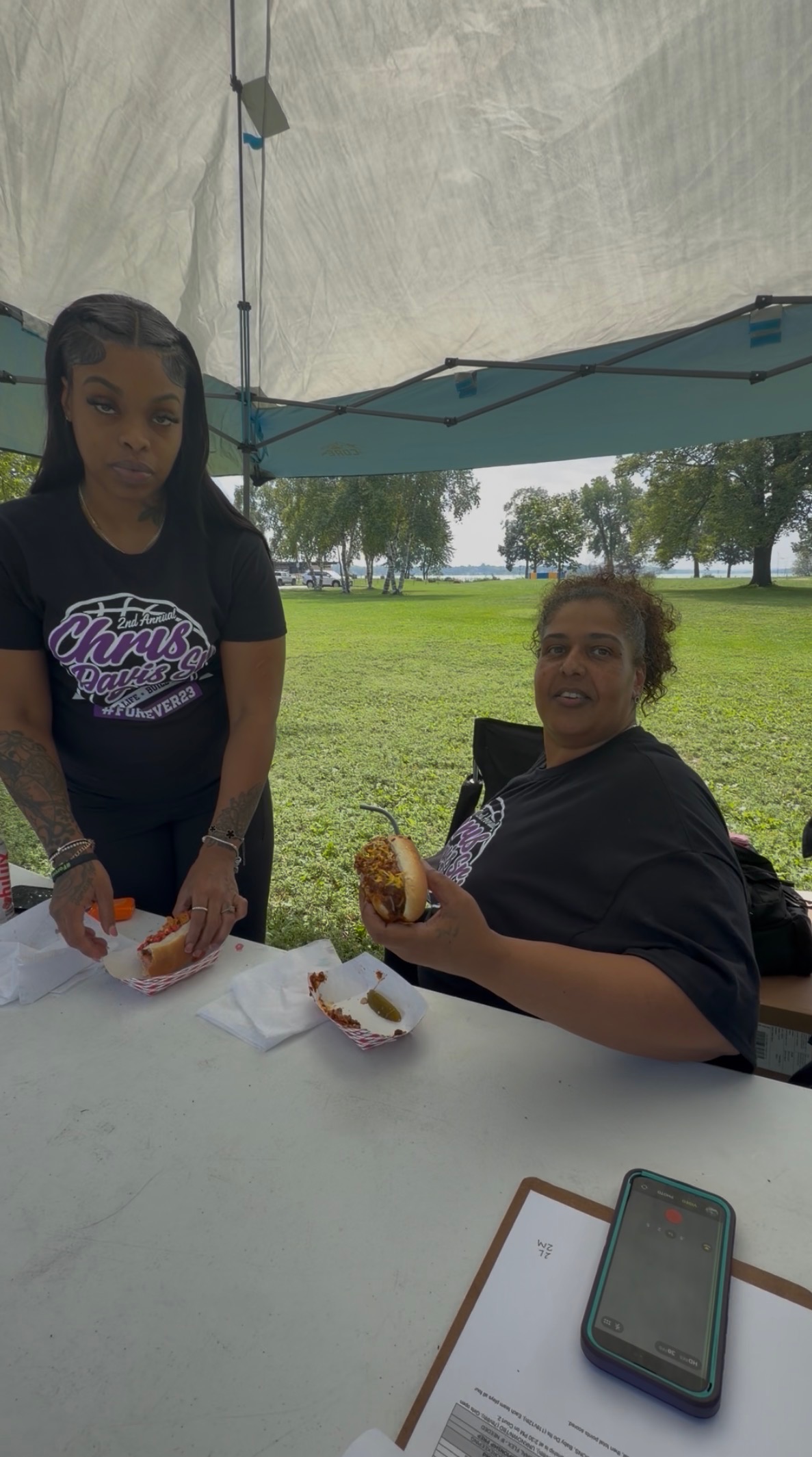 Two customers enjoying loaded chili dogs at a community fundraiser tent
