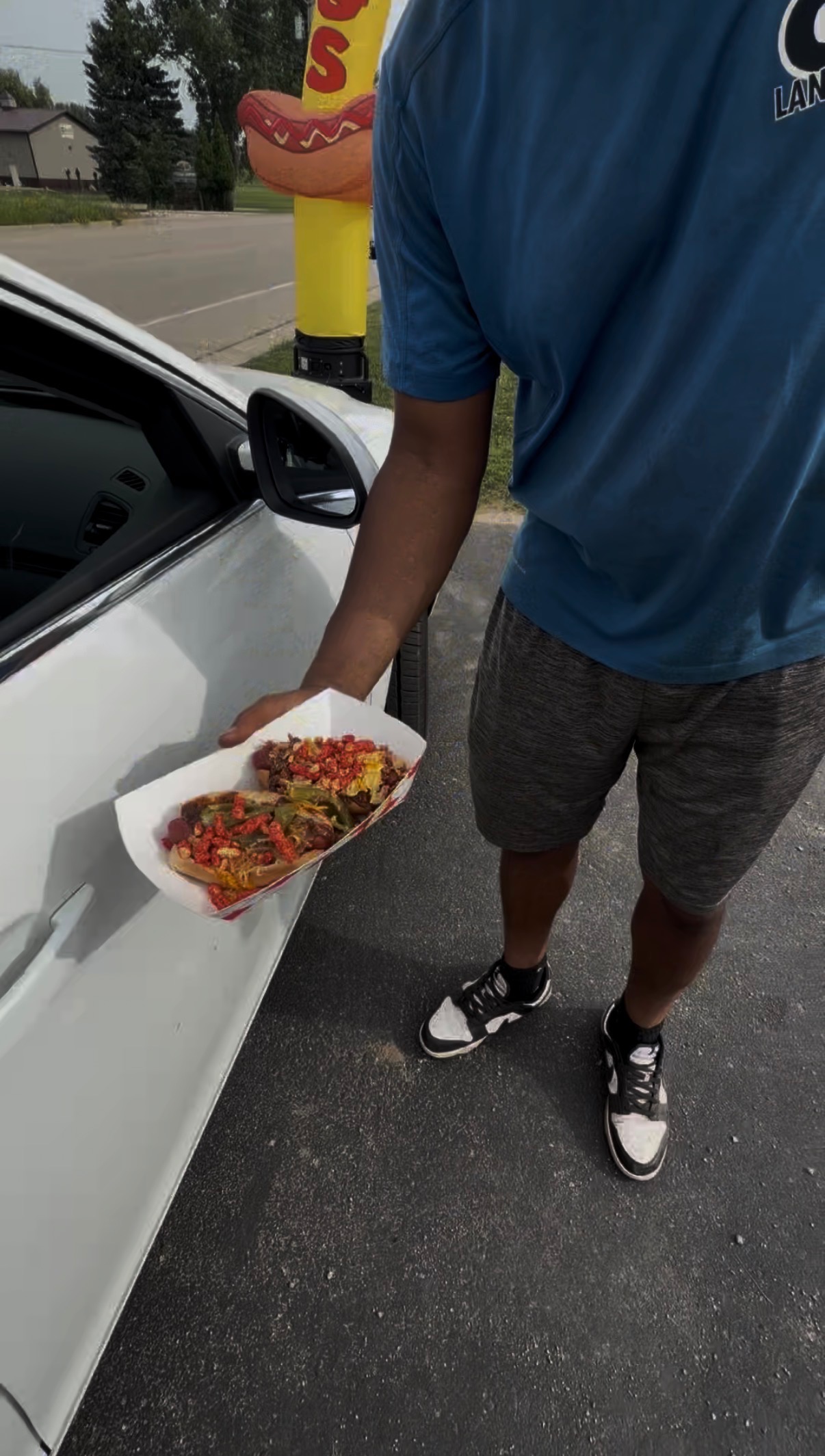 Customer holding a loaded hot dog tray next to a car outside the Papa Dogs stand