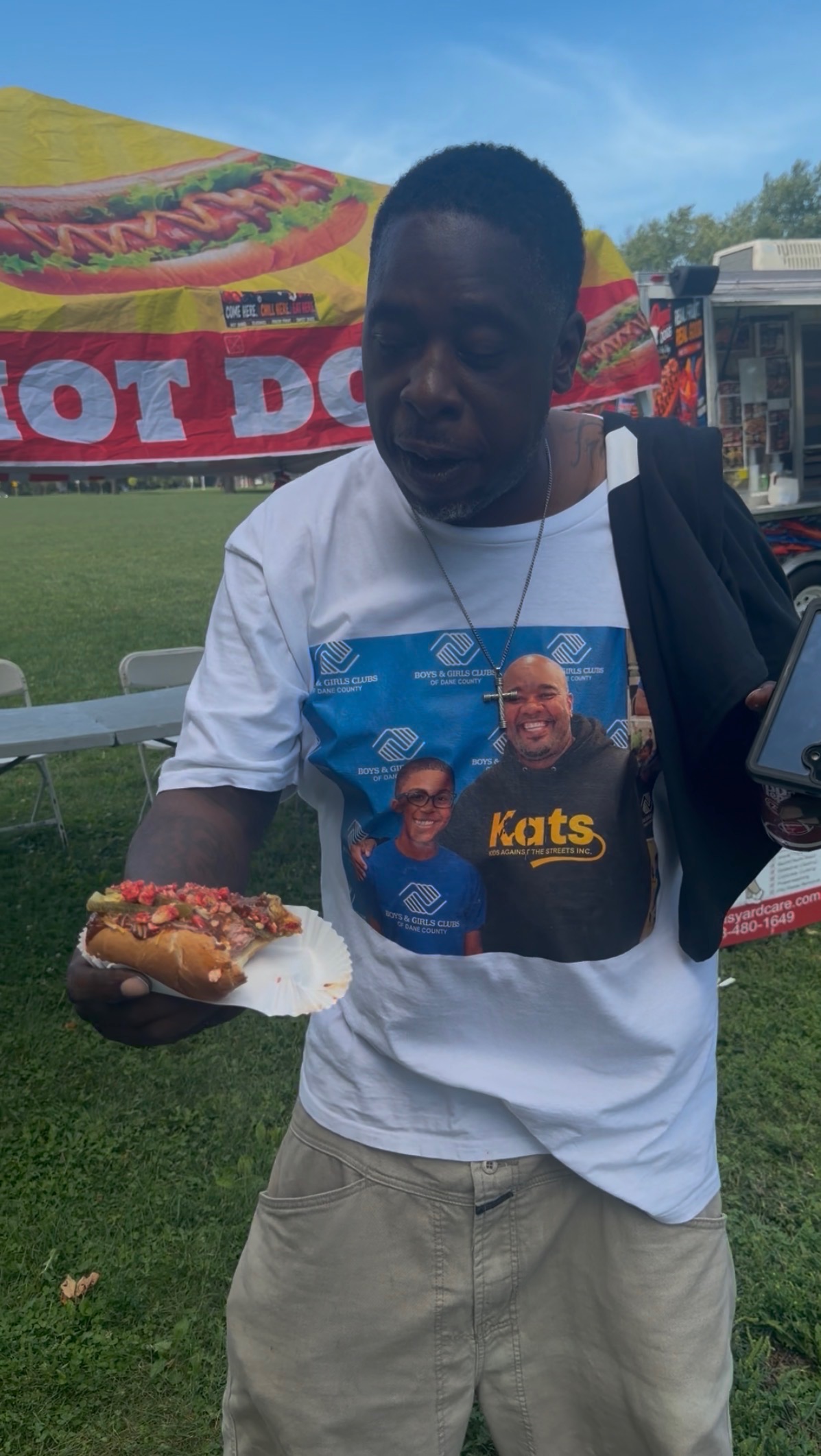 Customer holding a loaded Papa Dogs hot dog wearing a community charity shirt