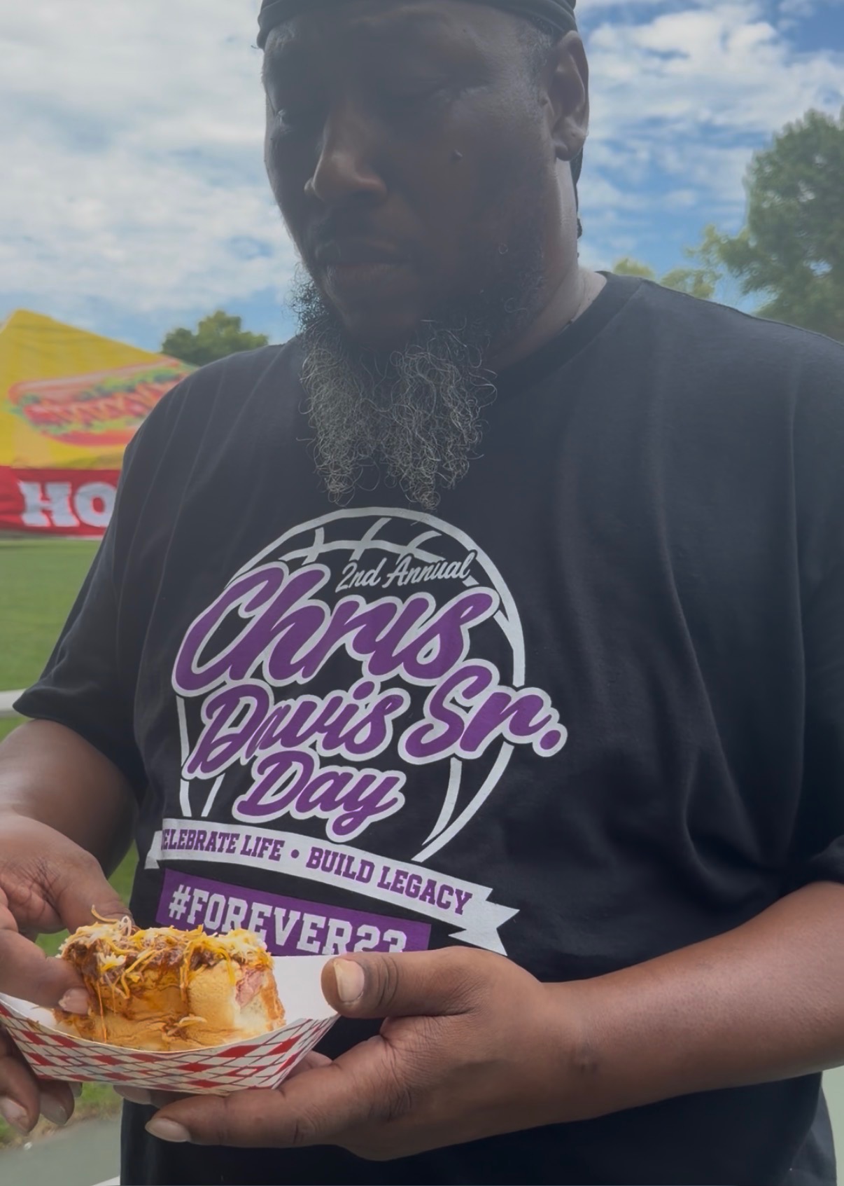 Community member at Chris Davis Sr. Day event holding a loaded hot dog