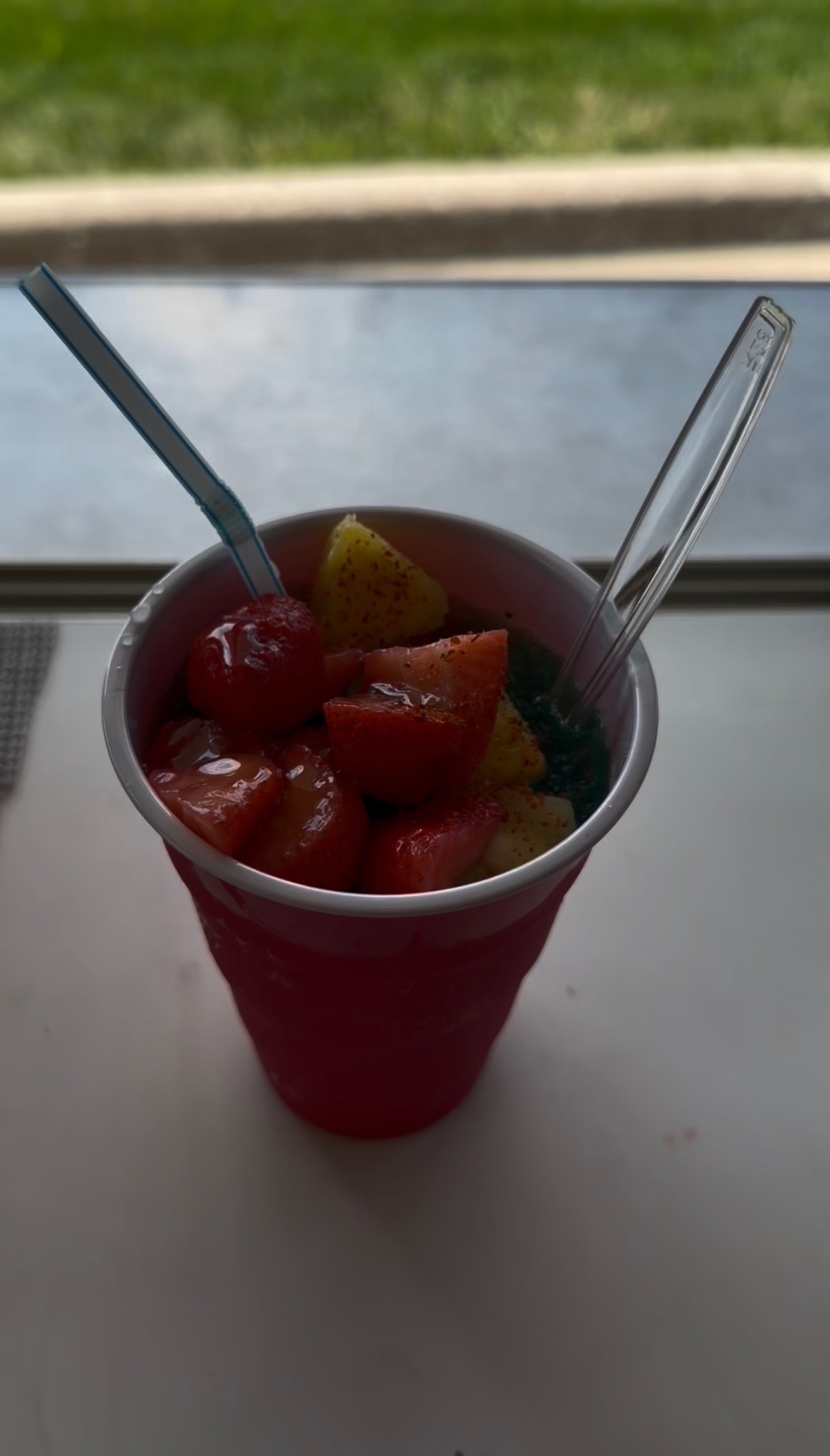Fresh fruit cup with strawberries and pineapple topped with Tajín in a red cup