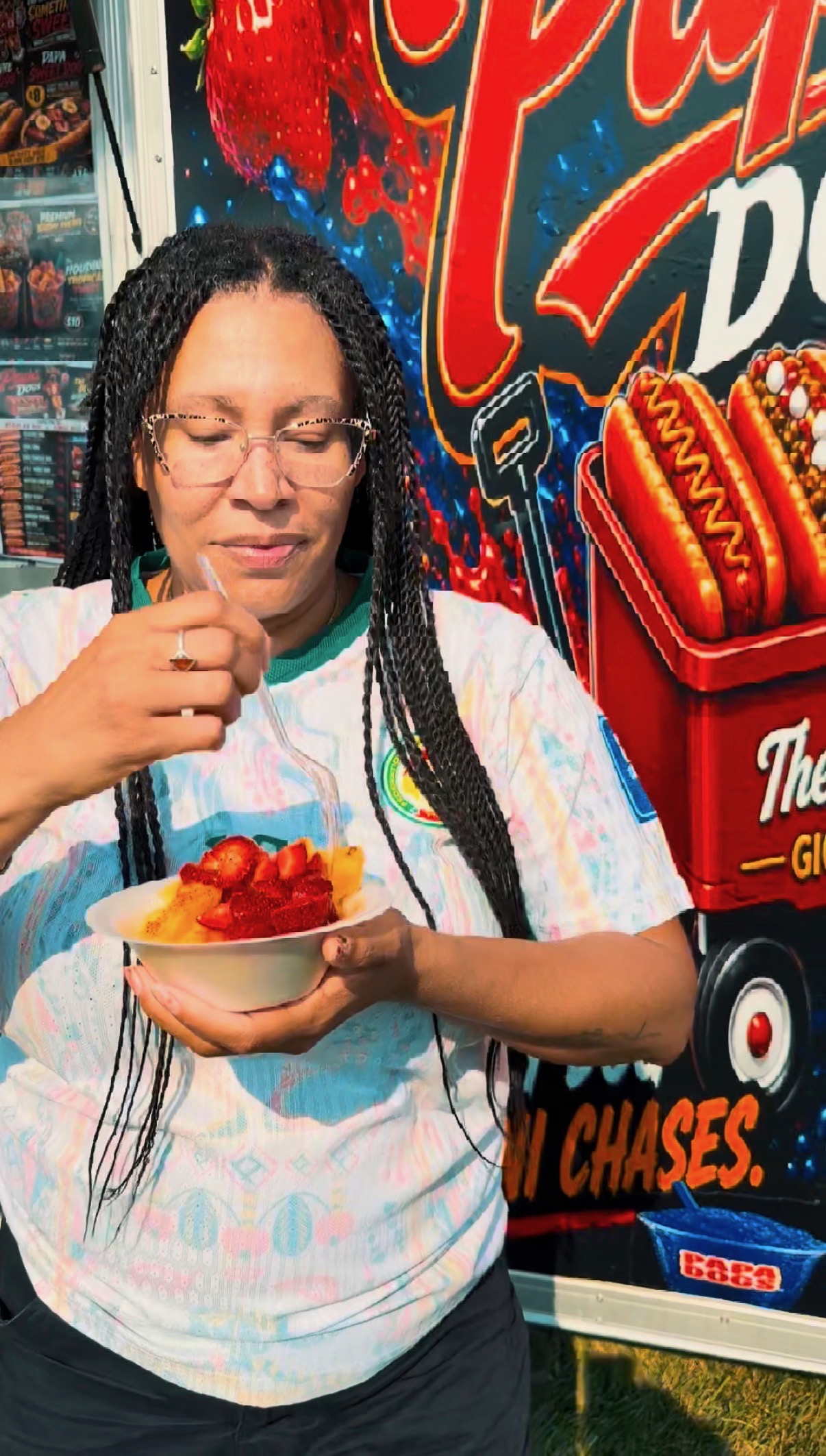 Customer enjoying a fresh fruit bowl with strawberries and pineapple in front of the Papa Dogs trailer mural