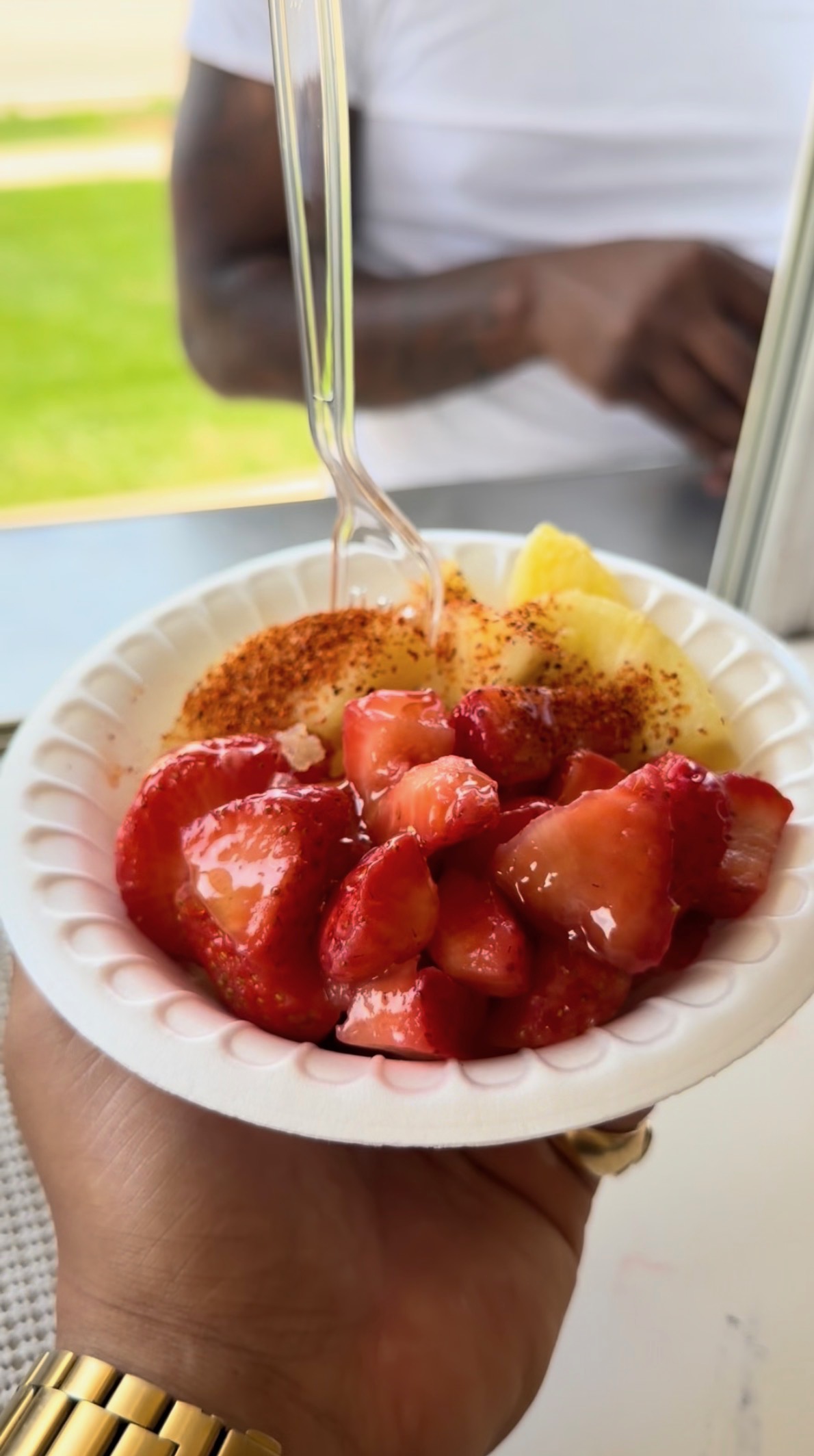 Customer holding a fresh fruit bowl with strawberries and pineapple topped with Tajín