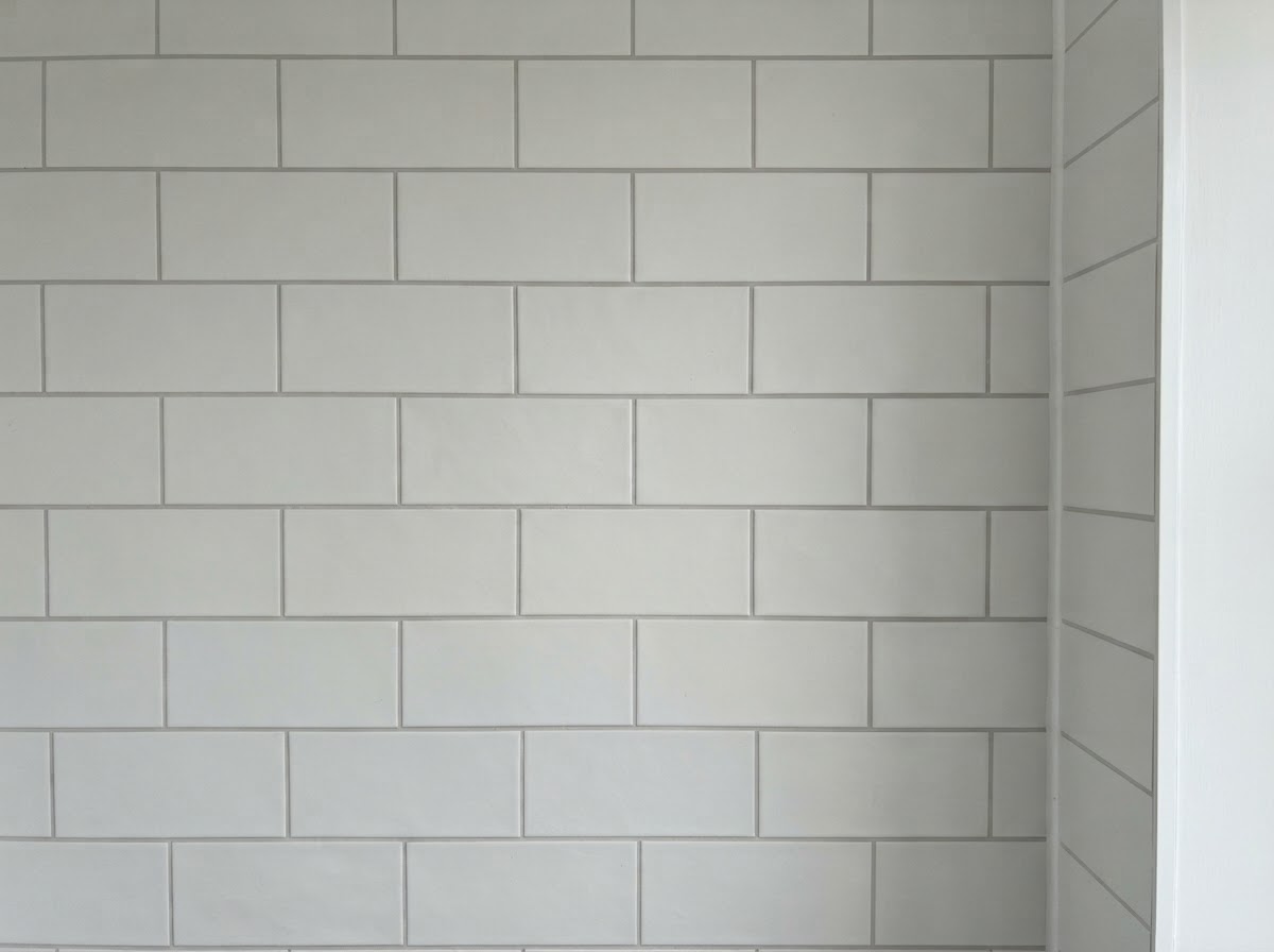 Completed sealed shower with fresh light-grey grout and clear silicone corner joins, white subway tiles laid horizontally in a brick pattern