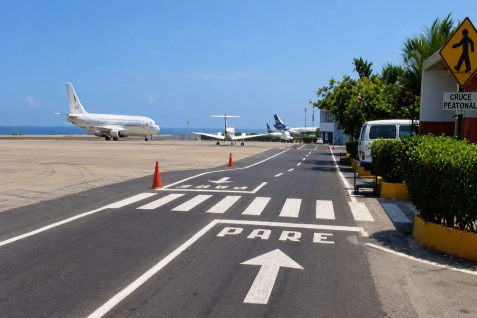 Vía interna de servicio aeroportuario debidamente demarcada con señalización horizontal ('PARE', flechas direccionales y paso peatonal) adyacente a la plataforma comercial de aeronaves
