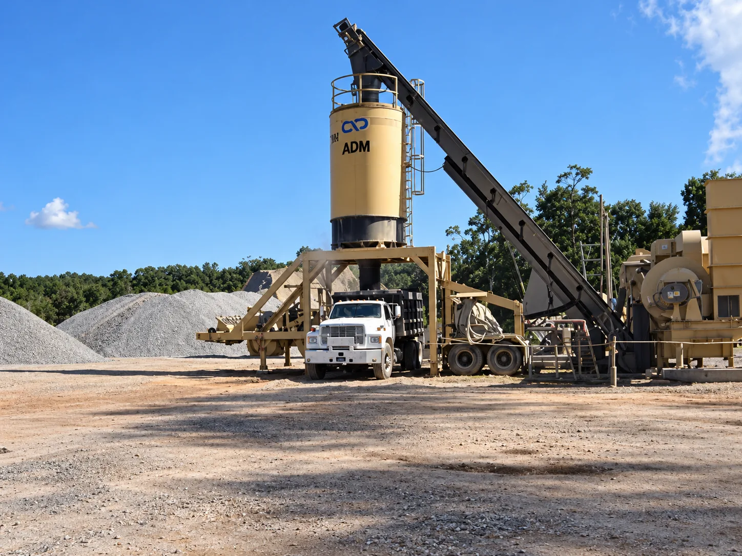 Silo vertical de almacenamiento y descarga de mezcla asfáltica ADM con camión volquete en patio operativo y acopio clasificado de agregados pétreos