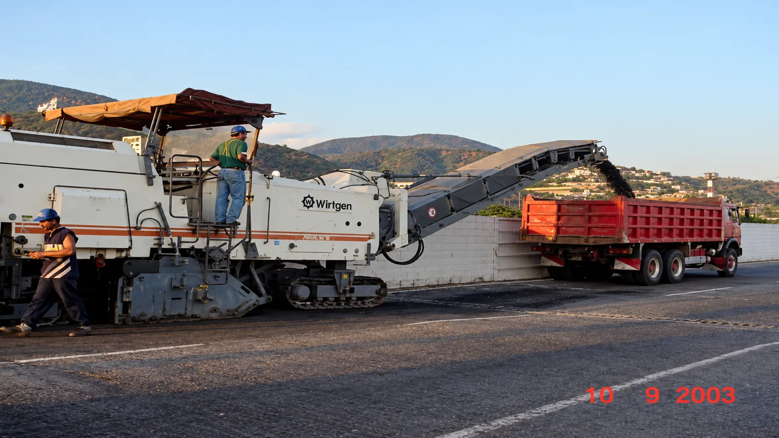 Fresadora pesada sobre orugas Wirtgen retirando 15 cm de pavimento asfáltico deteriorado y cargando material directamente a camión volquete en la calzada perimetral (septiembre 2003)