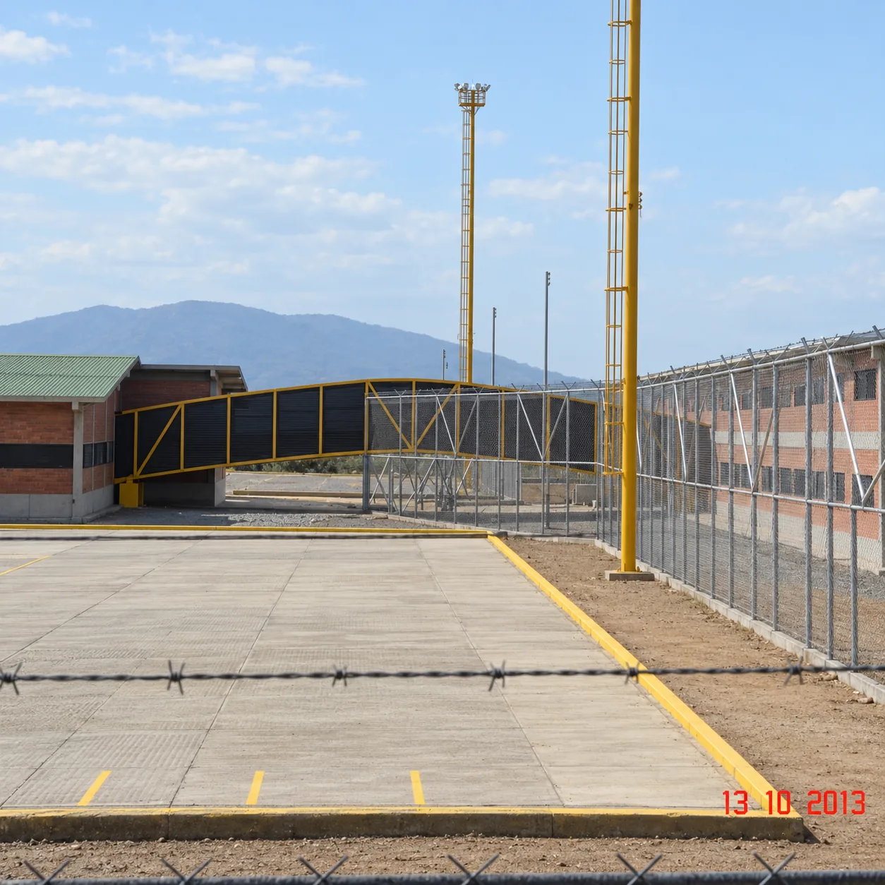 Patios pavimentados de circulación, puente peatonal de conexión enrejado, torres de iluminación y cerramientos de seguridad
