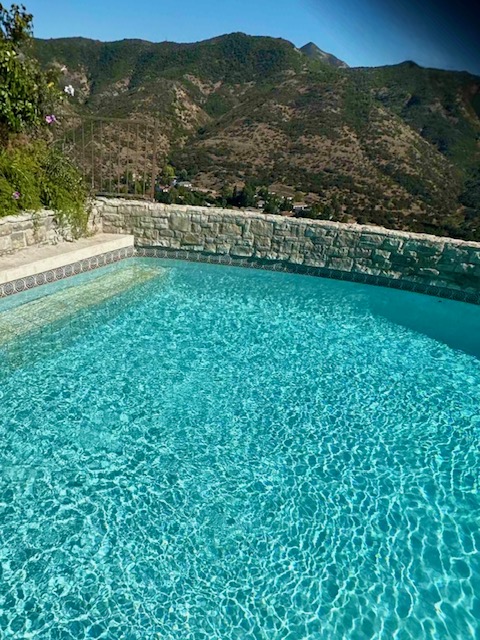 Swimming pool with clear turquoise water, stone coping, and mountain backdrop