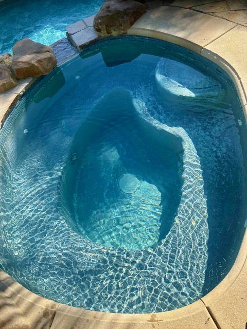 In-ground backyard spa with clear blue water and stone retaining wall