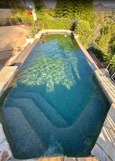 Narrow rectangular swimming pool with shallow entry steps and hillside greenery
