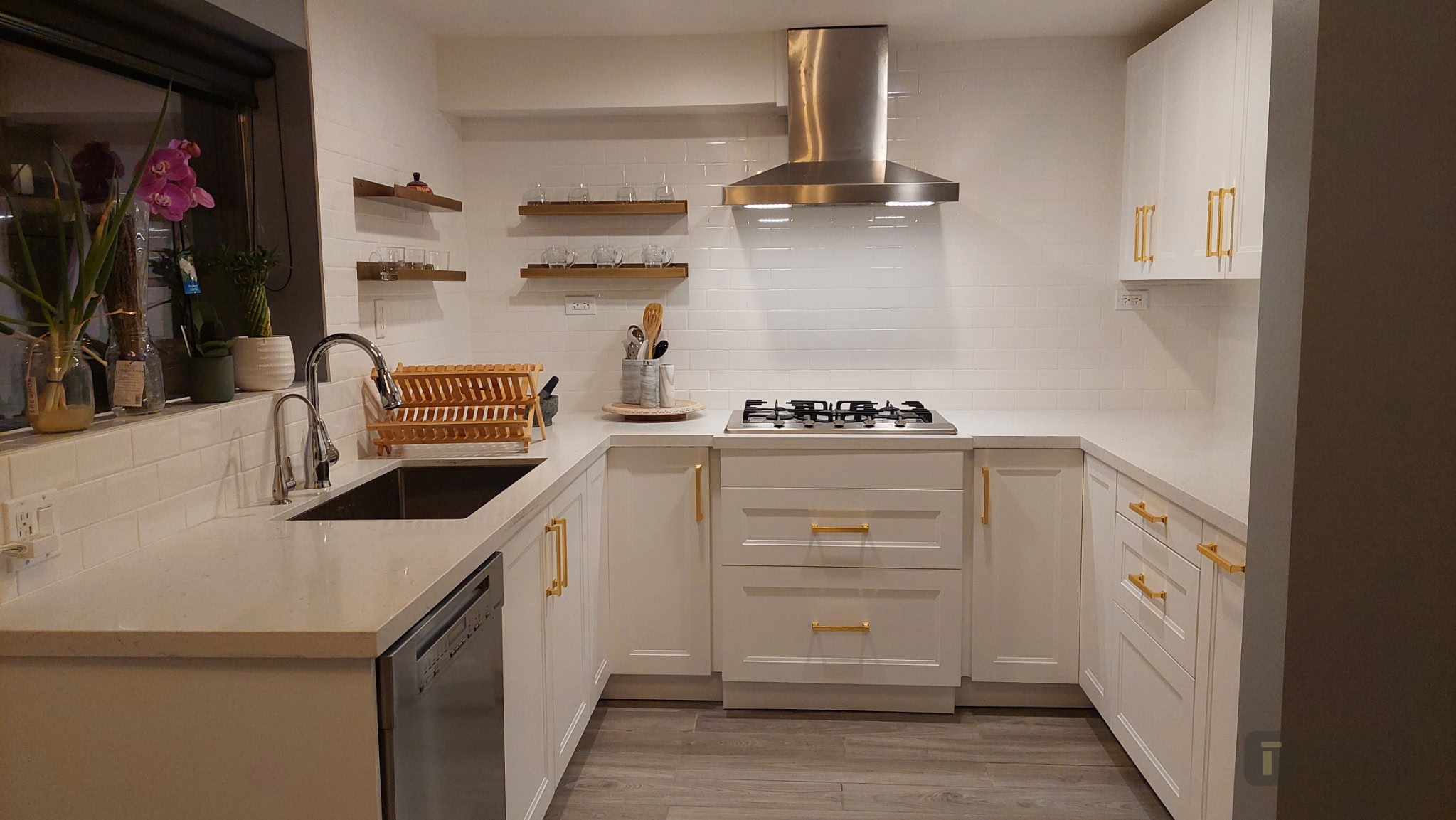 After: custom white quartz countertop with undermount sink, gas cooktop, and modern white cabinetry with brass hardware installed by Ideal Countertop