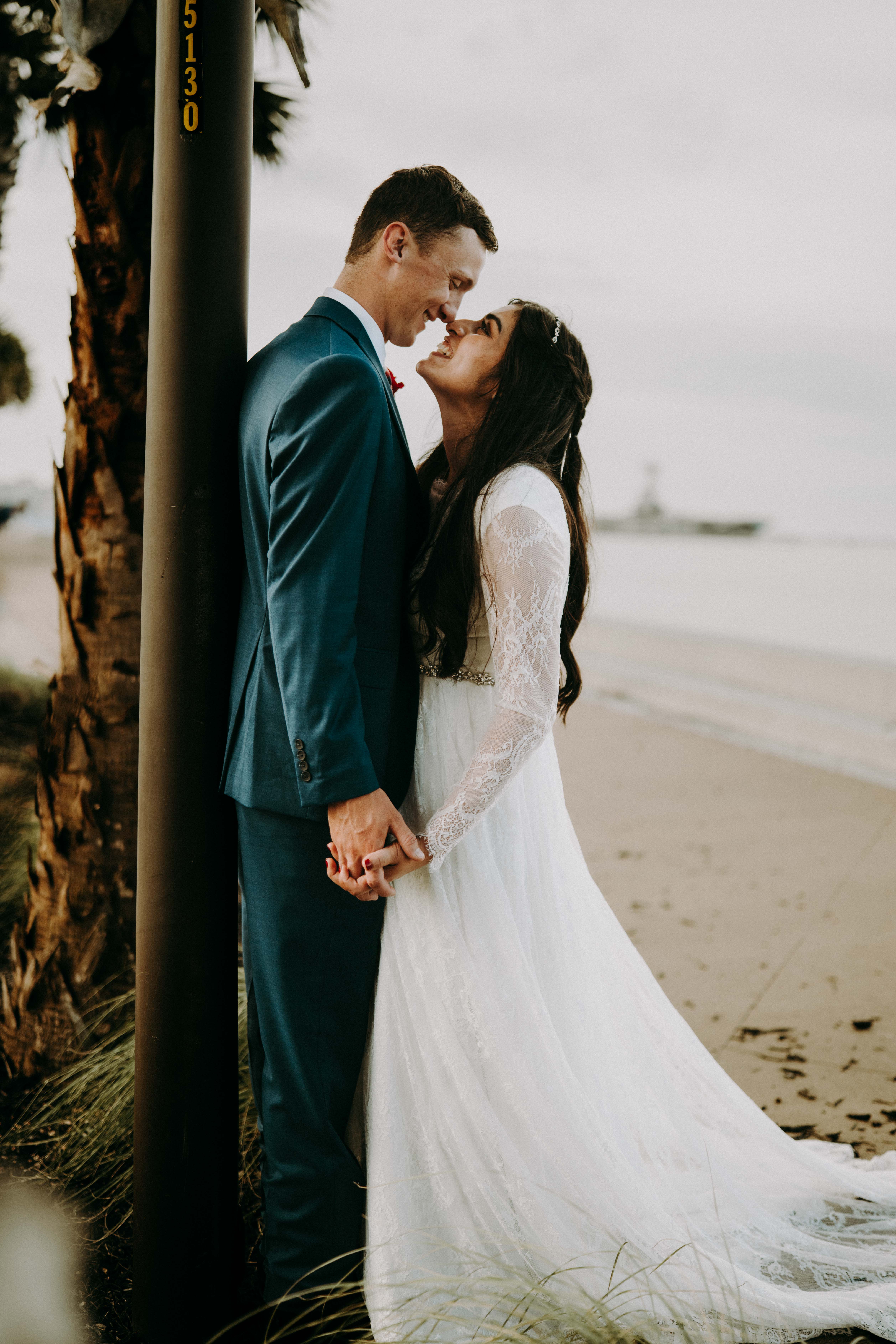 Bride and groom smiling together by a beach palm post