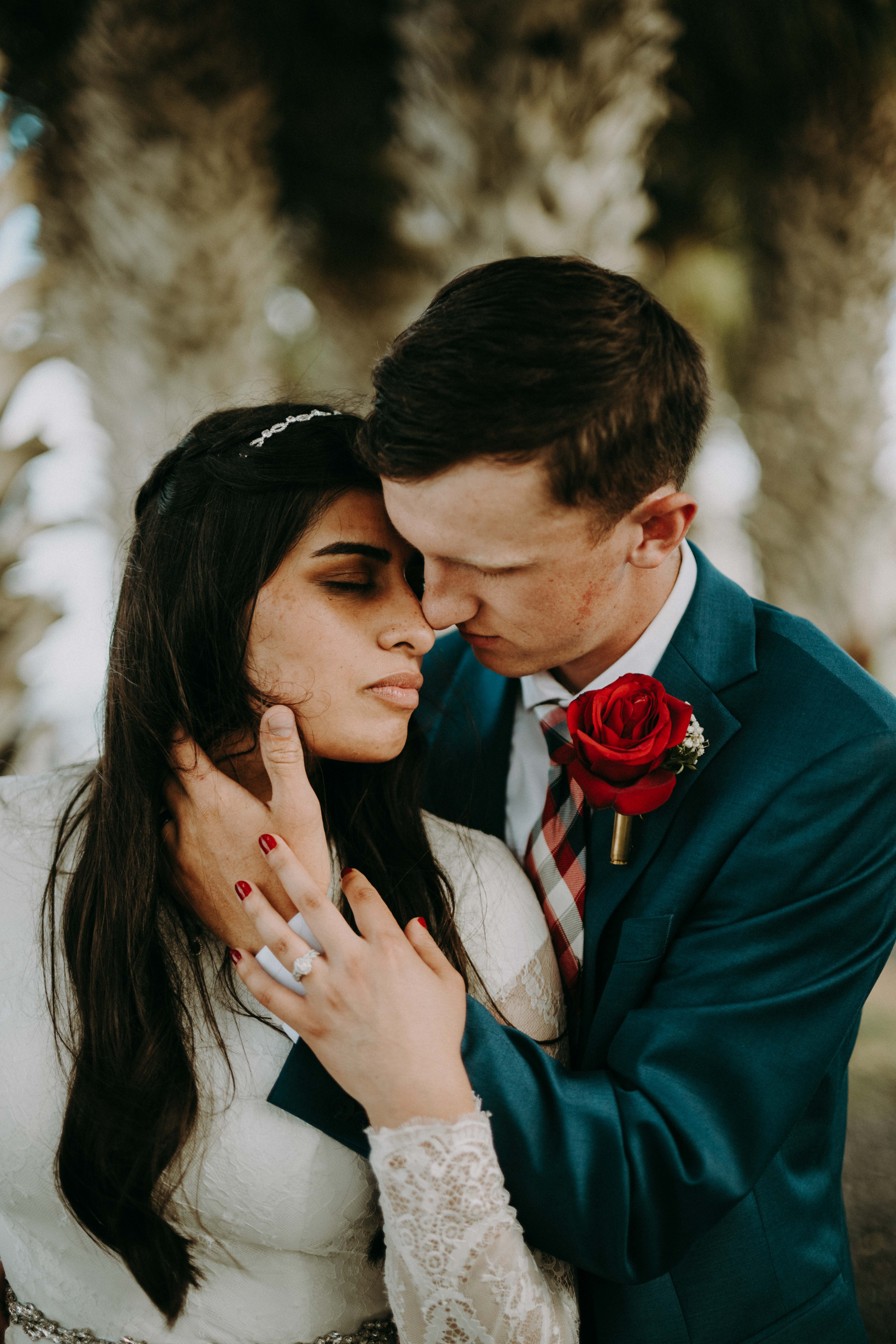 Groom gently touching the bride's face with a red rose boutonniere