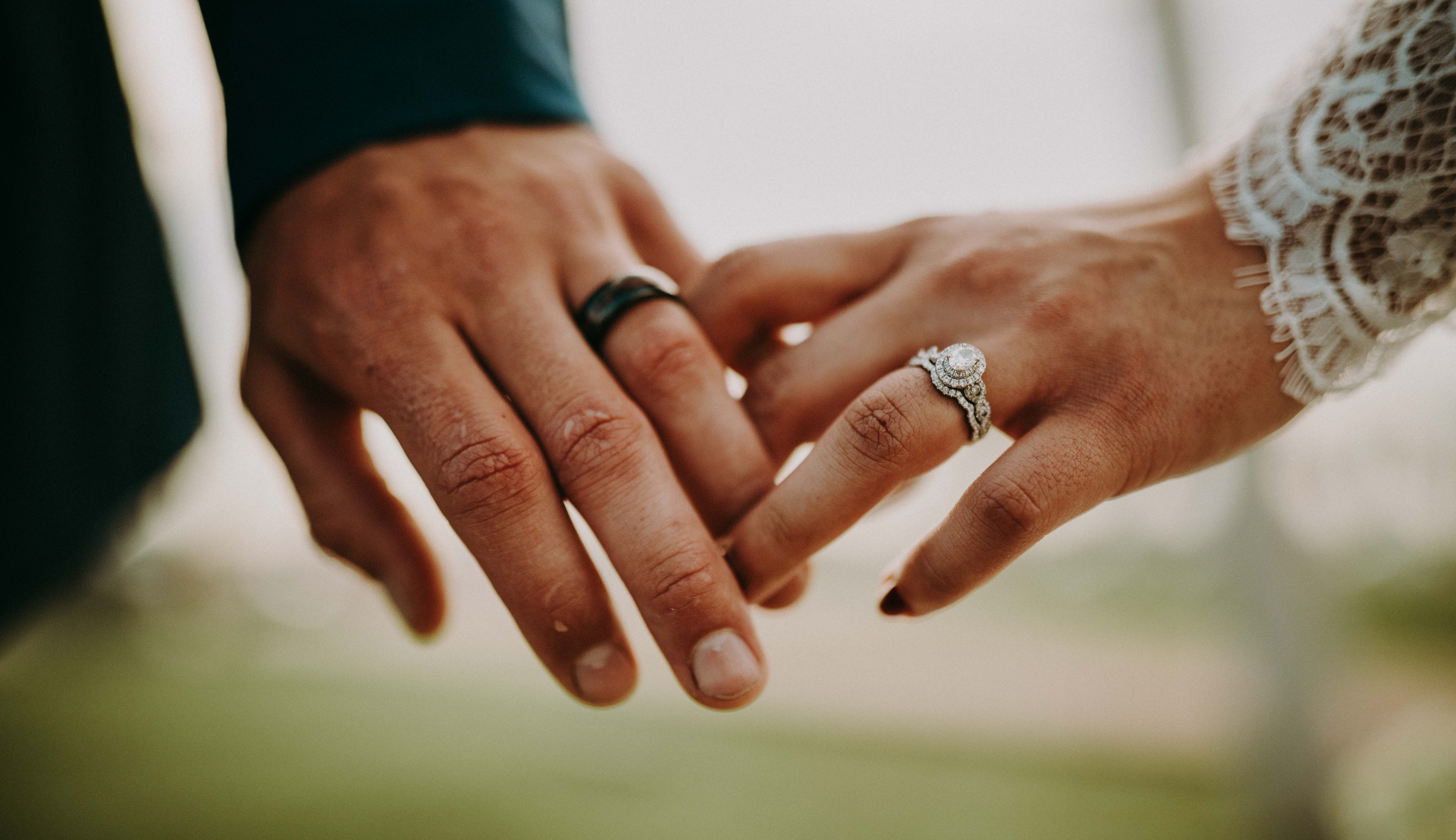 Intertwined hands showing groom wedding band and bride diamond engagement ring