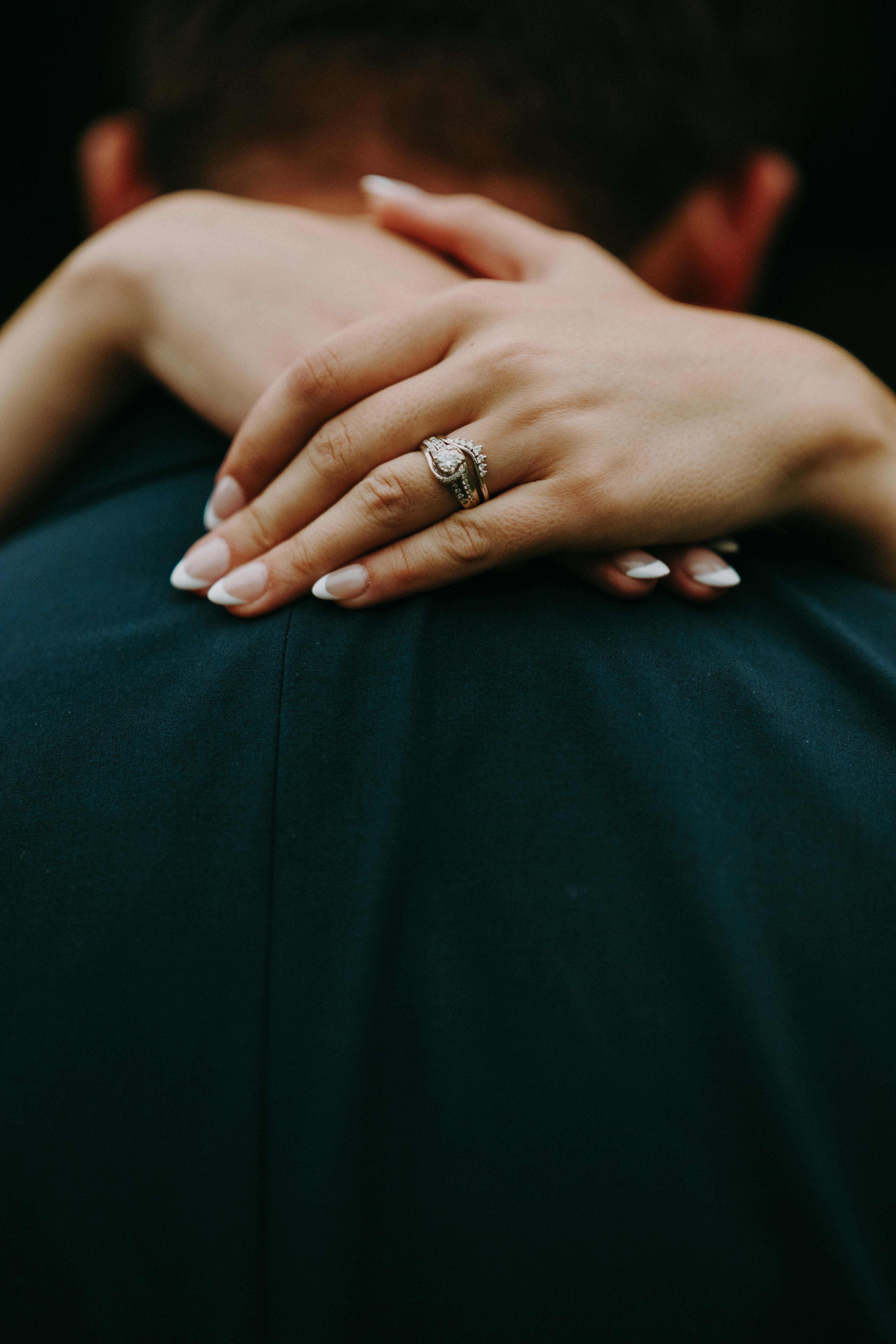 Close-up of bride embracing groom with engagement and wedding ring on shoulder