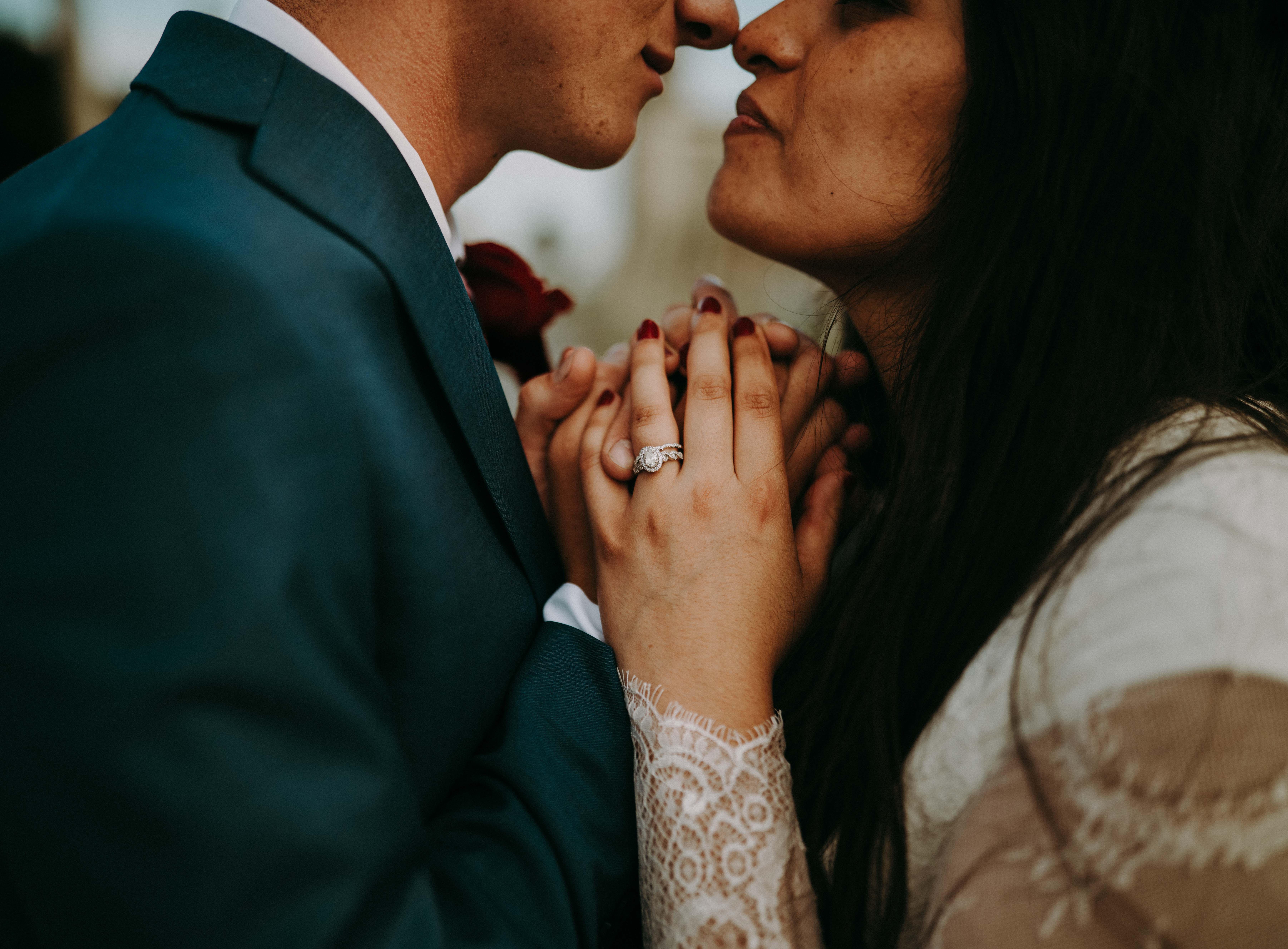 Intimate close-up moment with bride and groom holding hands near faces