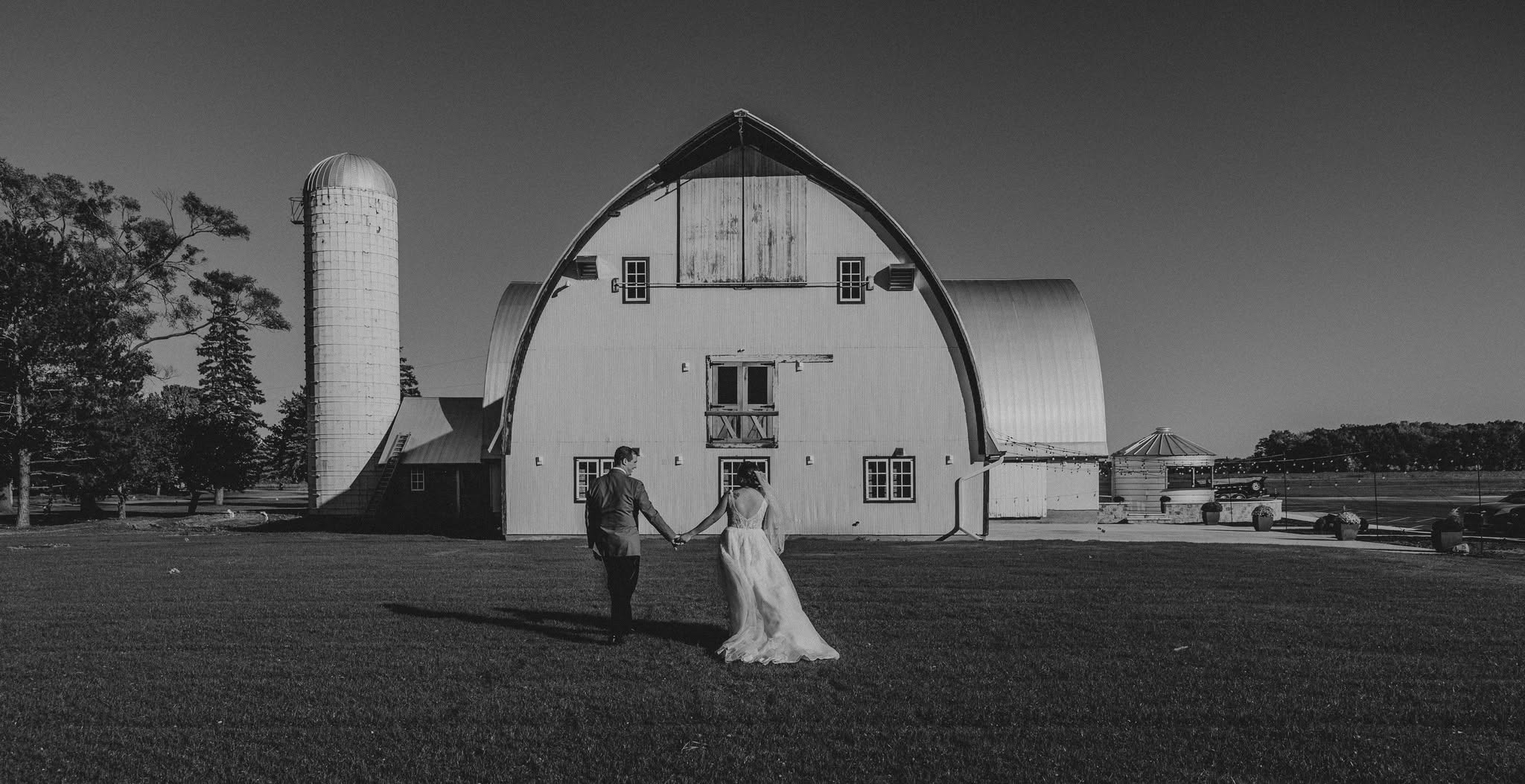 Couple walking hand in hand towards round barn at wedding