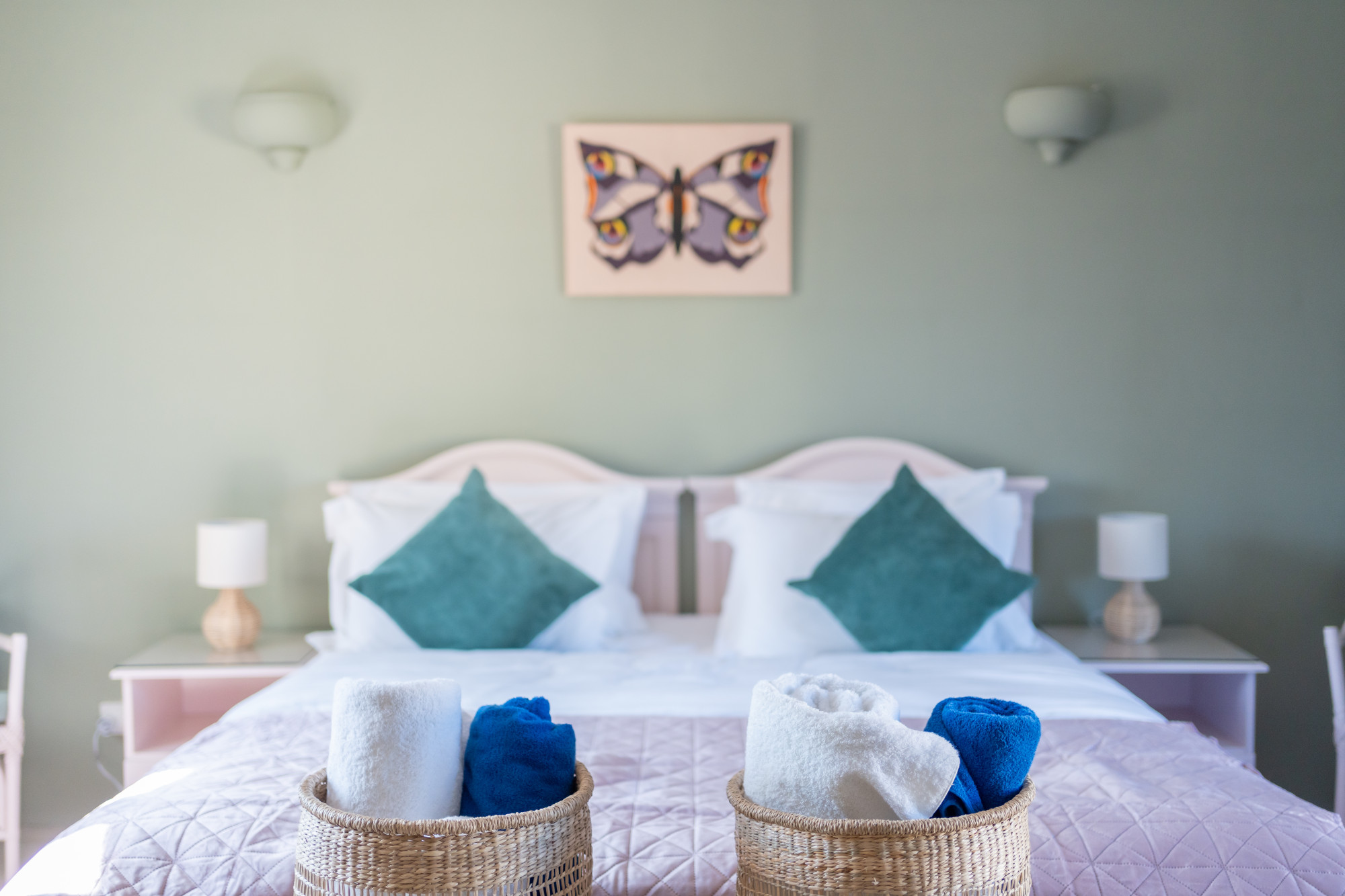 Tranquil bedroom suite with plush linens, woven towel baskets and butterfly wall art