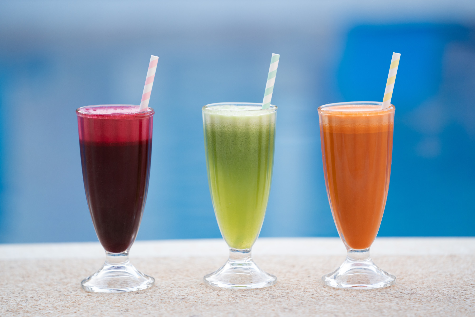 Trio of freshly pressed detox juices served poolside against blue waters