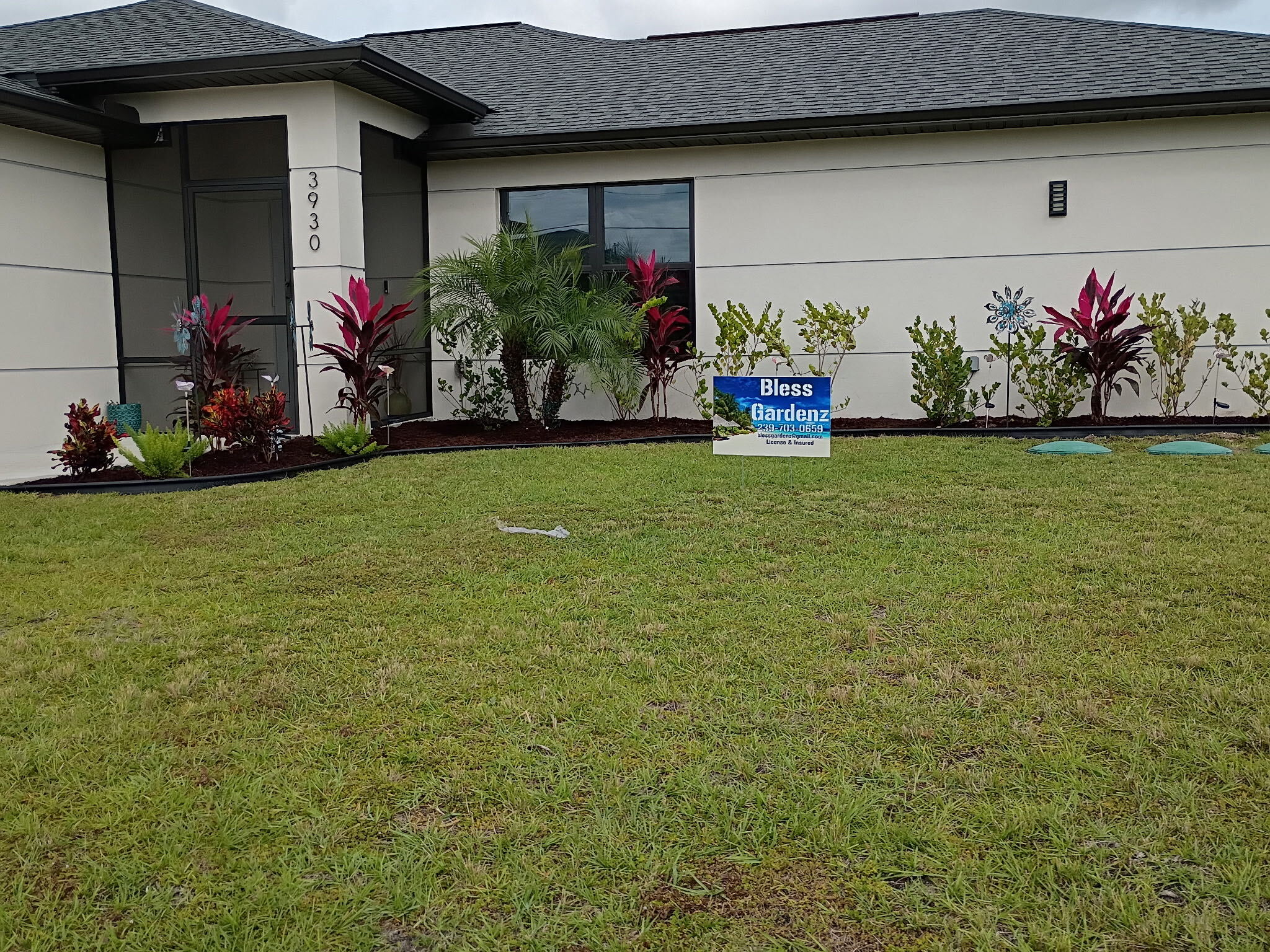 Finished front yard by Bless Gardenz with manicured green lawn, clean edging, tropical plant bed, and company yard sign in Fort Myers, FL
