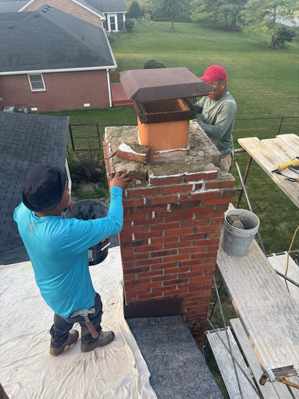 Masonry crew removing a failed chimney crown and loose brick before the rebuild