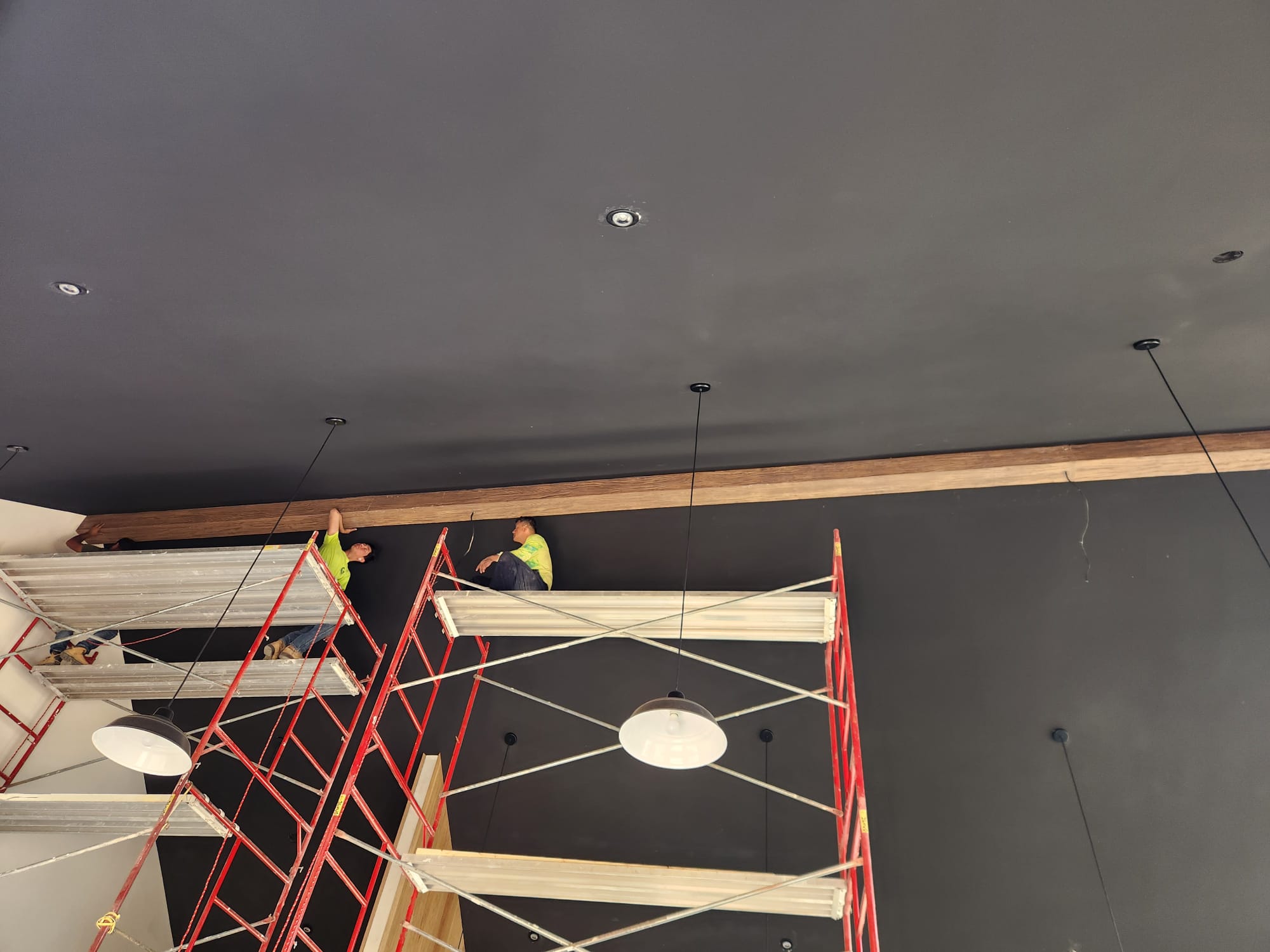Crafted Wood & Trim carpenters on scaffolding installing massive wood ceiling beam against charcoal ceiling in Winston-Salem NC